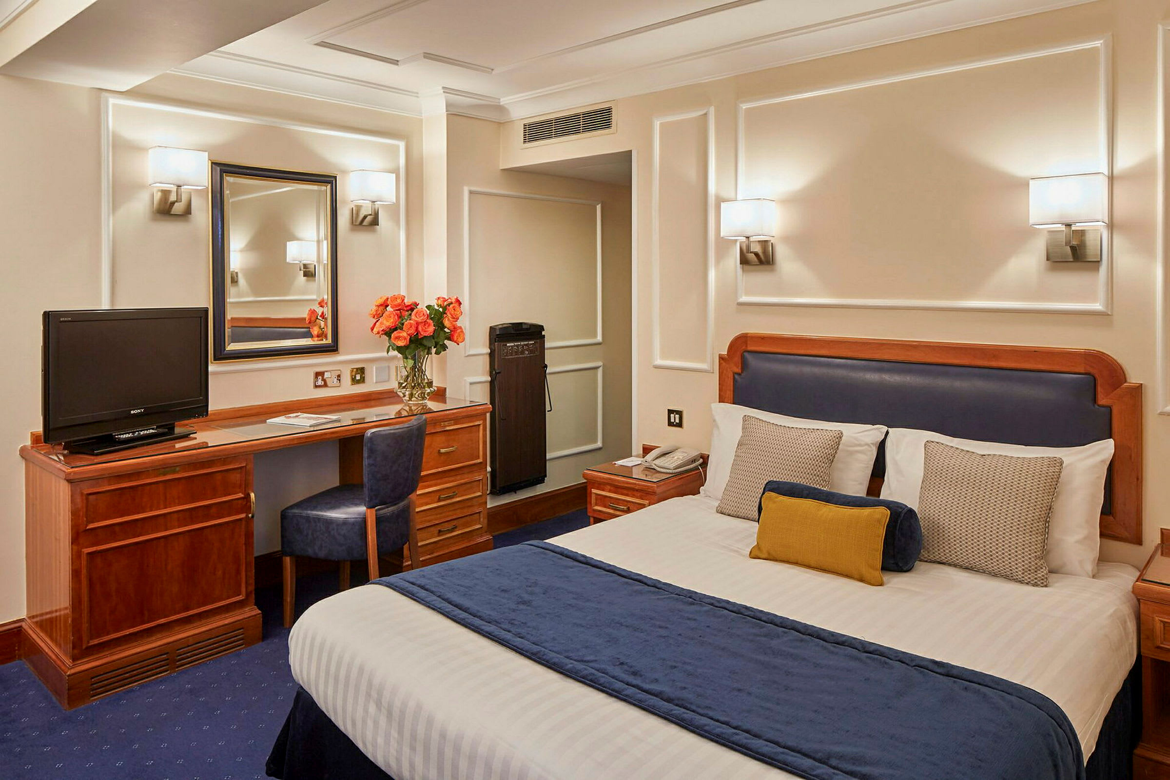Hotellrom med en seng, skrivebord, stol og speil. (AI-generert tekst)