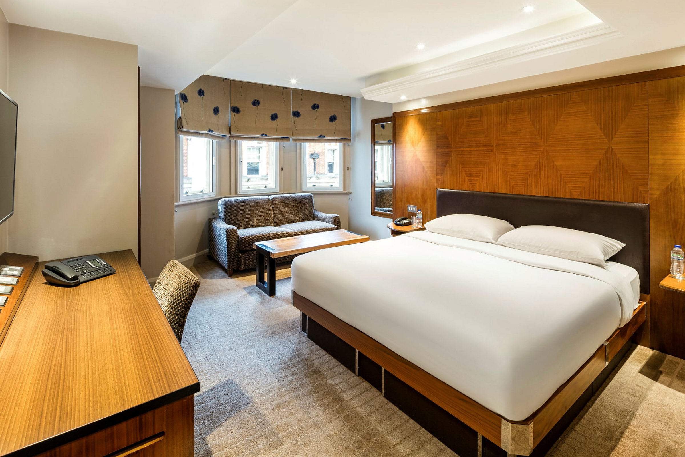 Bildet viser et hotellrom med en stor seng, en sofa og et skrivebord. (AI-generert tekst)