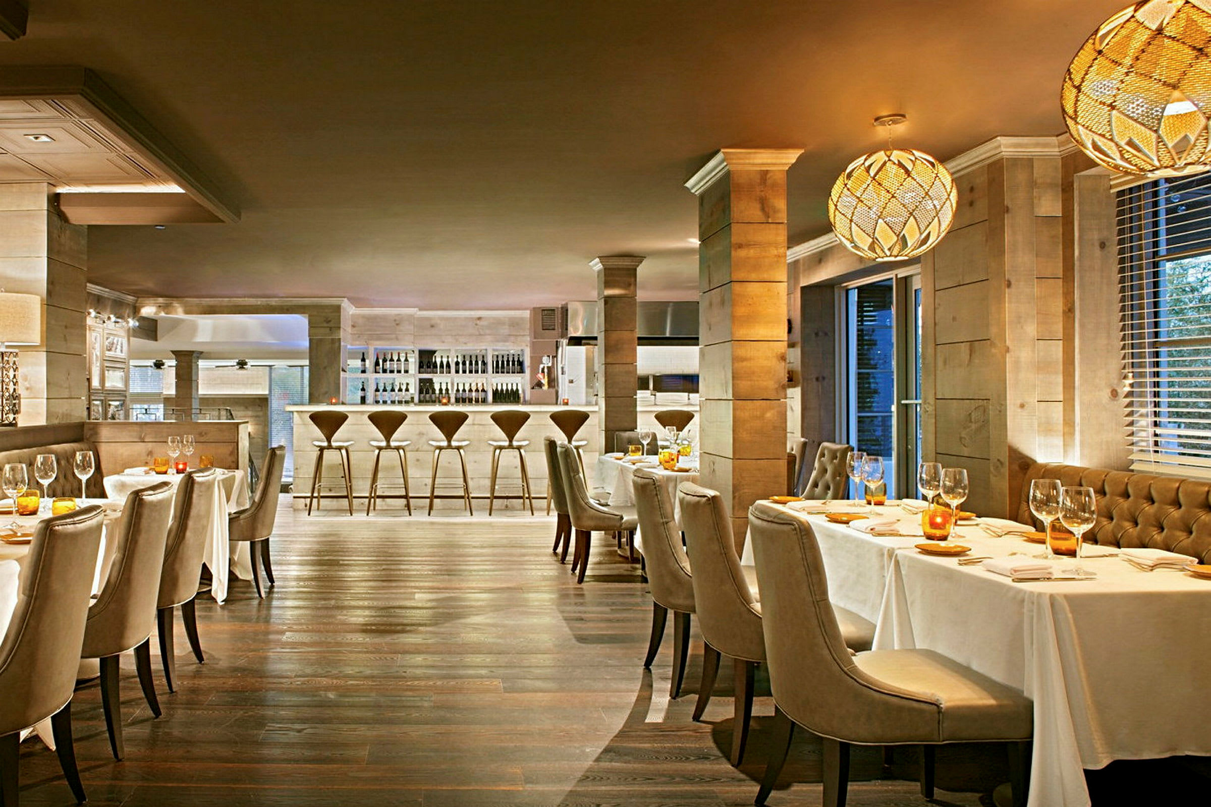 En elegant restaurant med bord dekket med hvite duker, stoppede stoler og en bardisk i bakgrunnen. (AI-generert tekst)