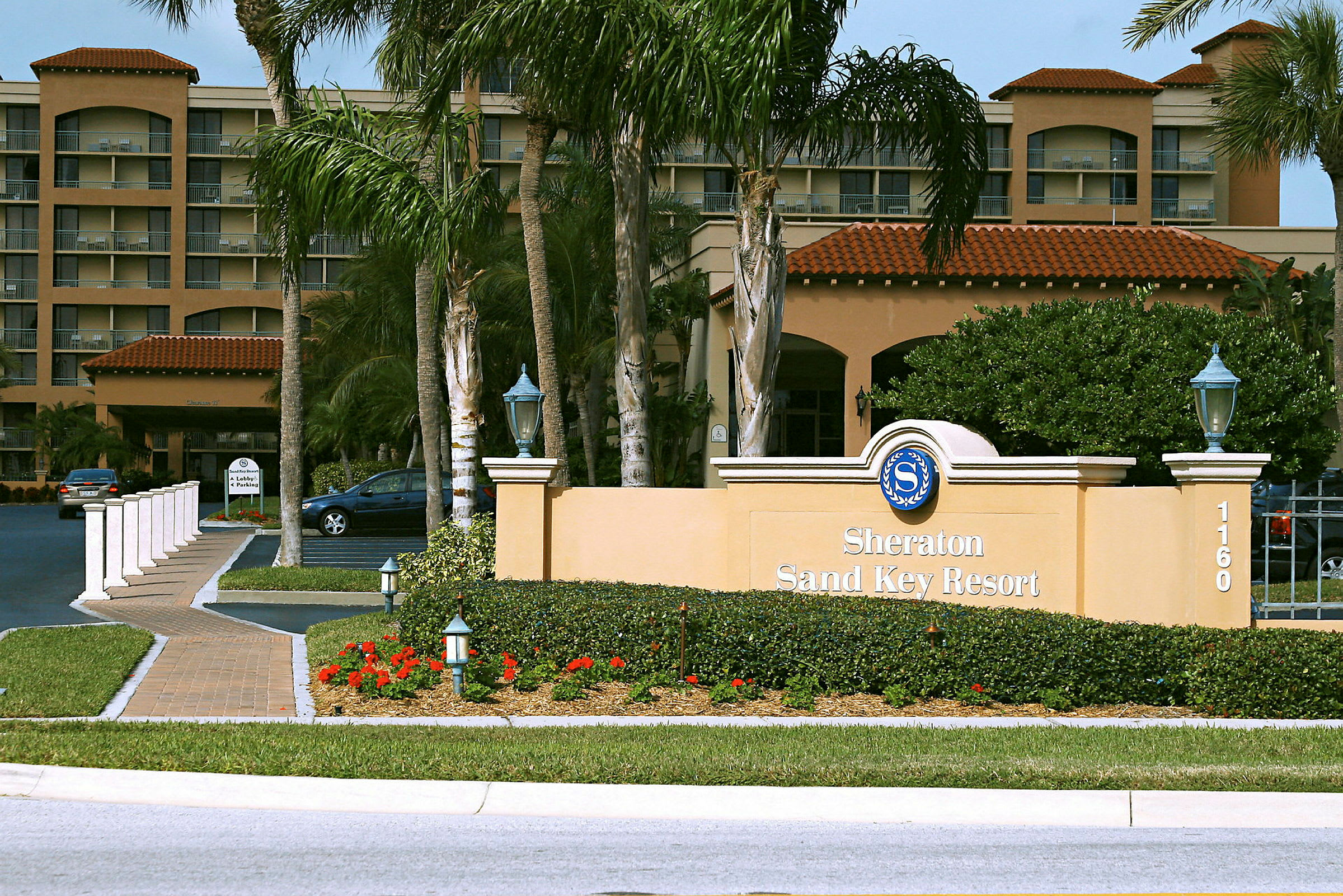 Et hotell med et skilt som sier "Sheraton Sand Key Resort" omgitt av grøntområder og palmer. (AI-generert tekst)