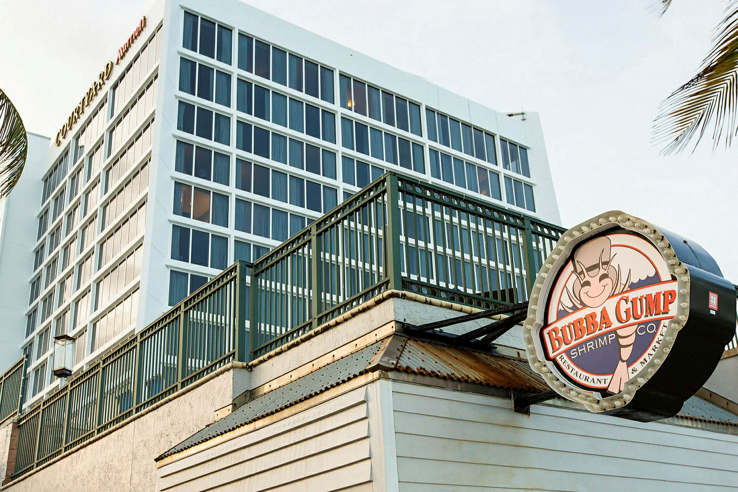 En moderne bygning i bakgrunnen med store vinduer, og i forgrunnen et skilt for restauranten Bubba Gump Shrimp Co. (AI-generert tekst)