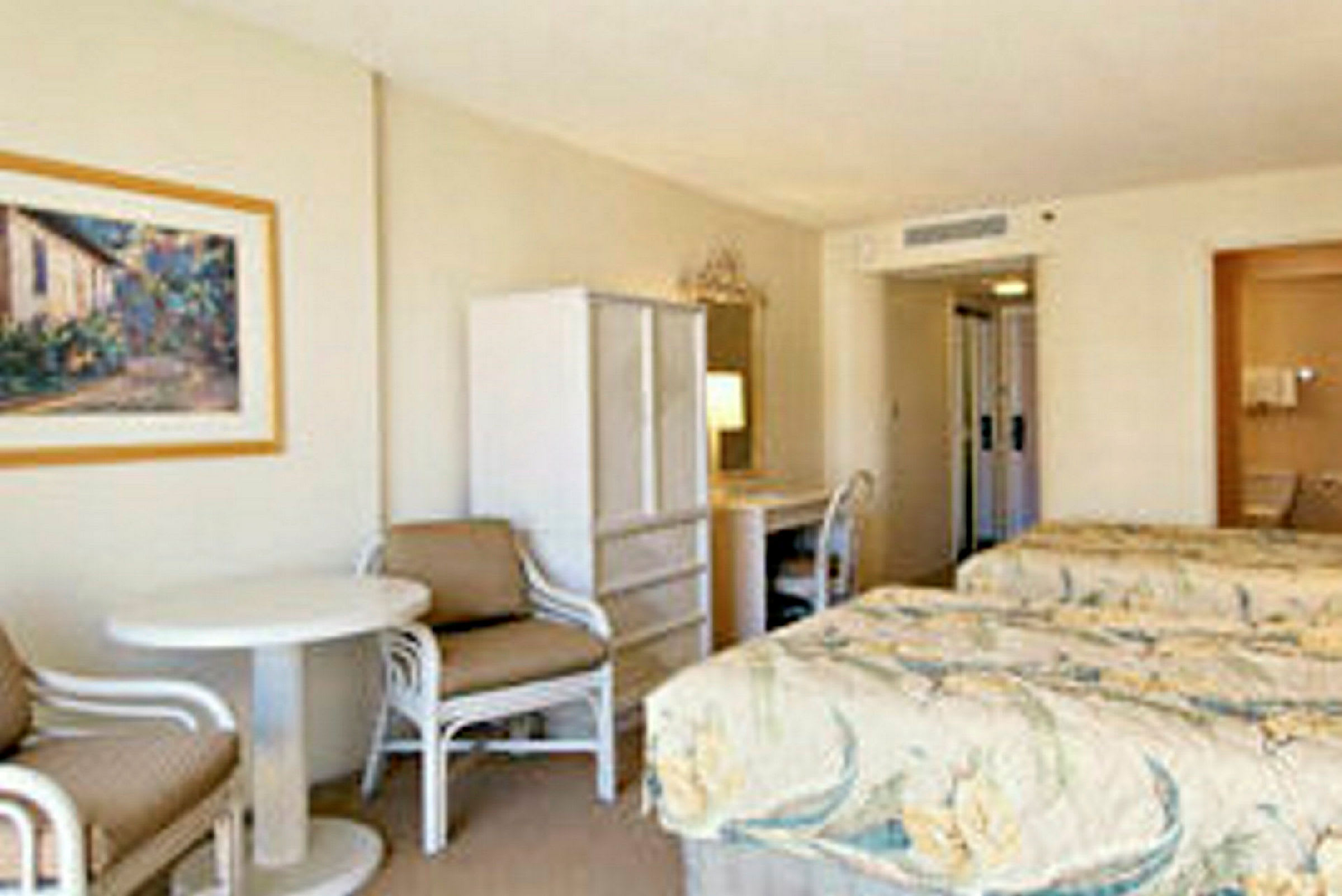 Hotellrom med to senger, et lite bord med stoler og et skap. (AI-generert tekst)