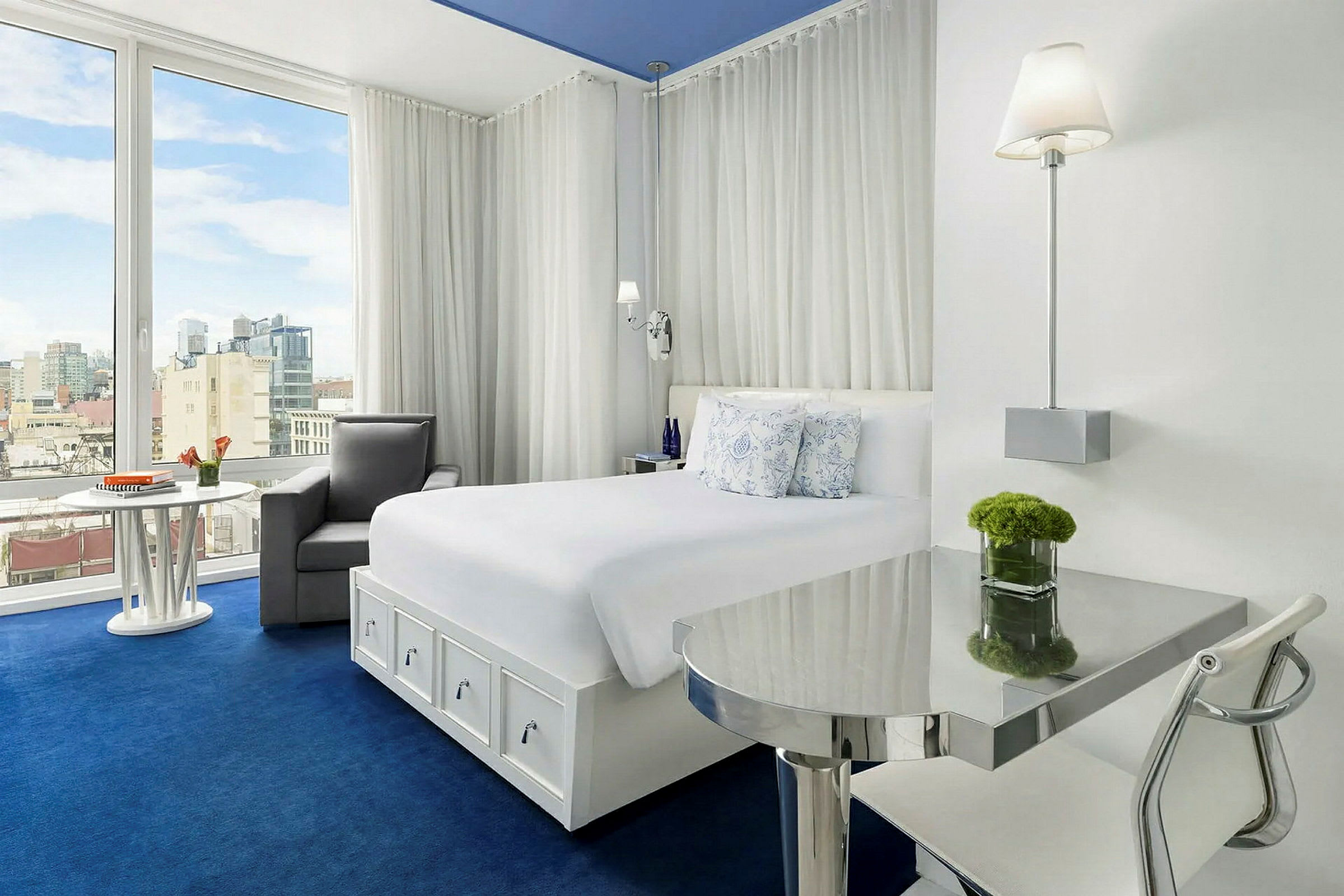 Et lyst og moderne hotellrom med hvitt interiør og en stor seng. Rommet har et vindu med utsikt over en by. (AI-generert tekst)