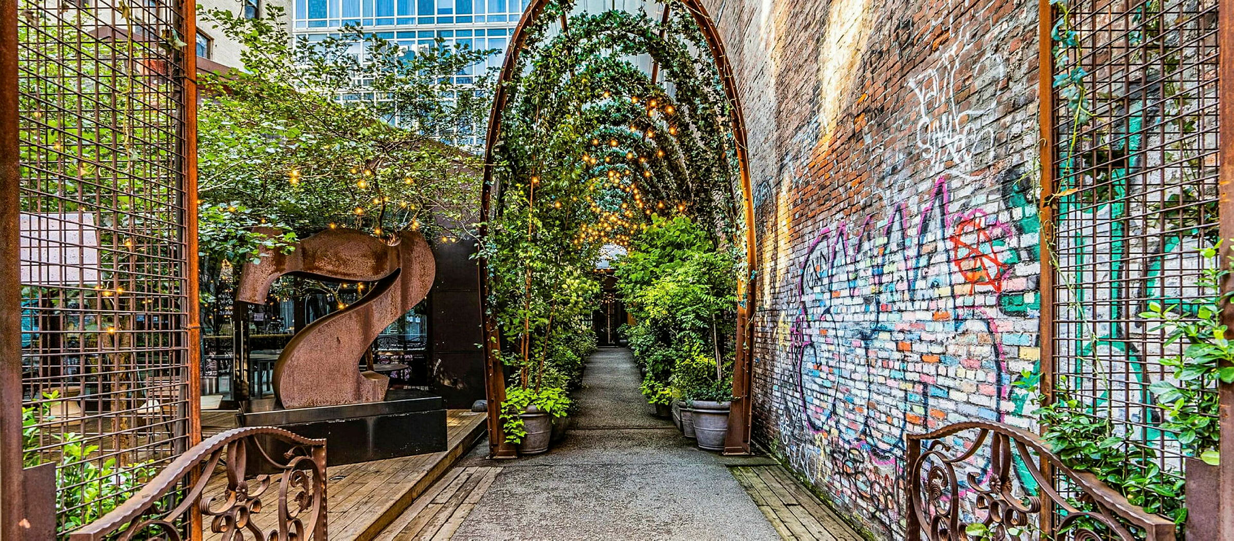 En gate med en overbygd gang og planter samt en mursteinvegg merket med graffiti. (AI-generert tekst)