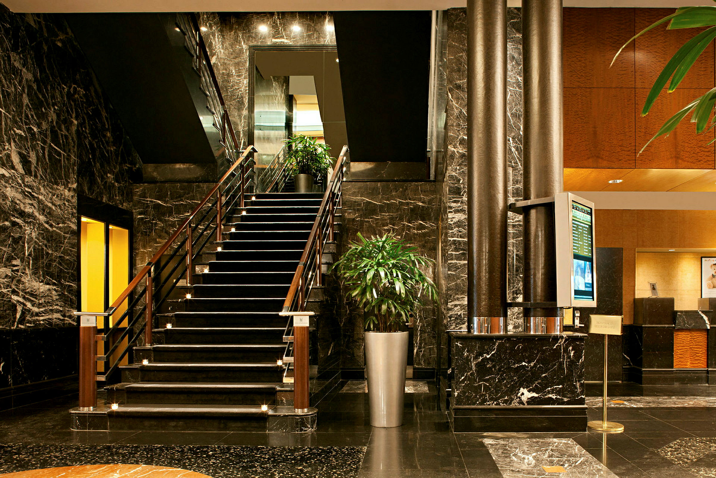En hotelllobby med en trapp, marmorflater og grønne planter. (AI-generert tekst)