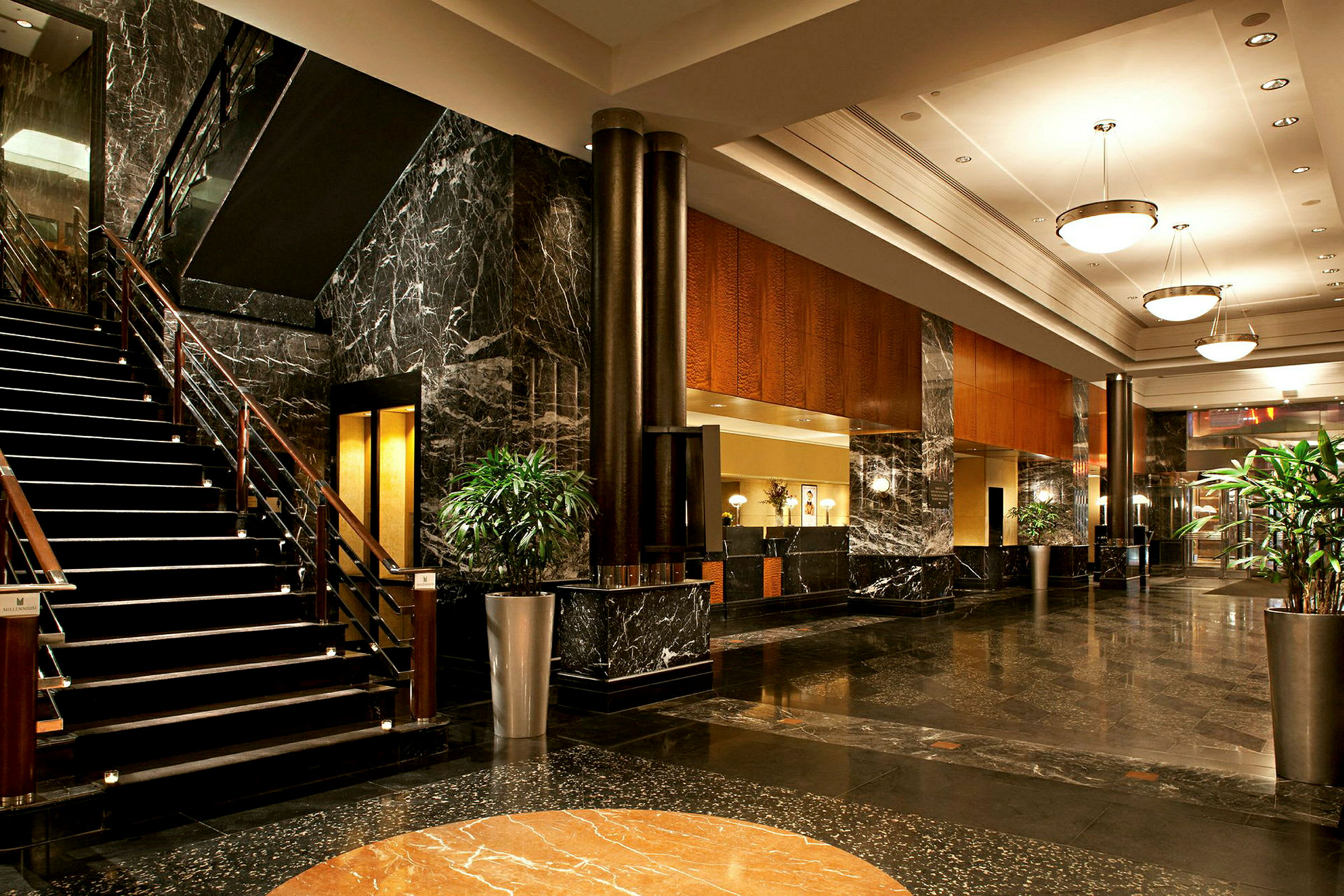 Bilde av hotellets lobby med marmorgulv, en trapp, sofaer og plantearrangement. (AI-generert tekst)