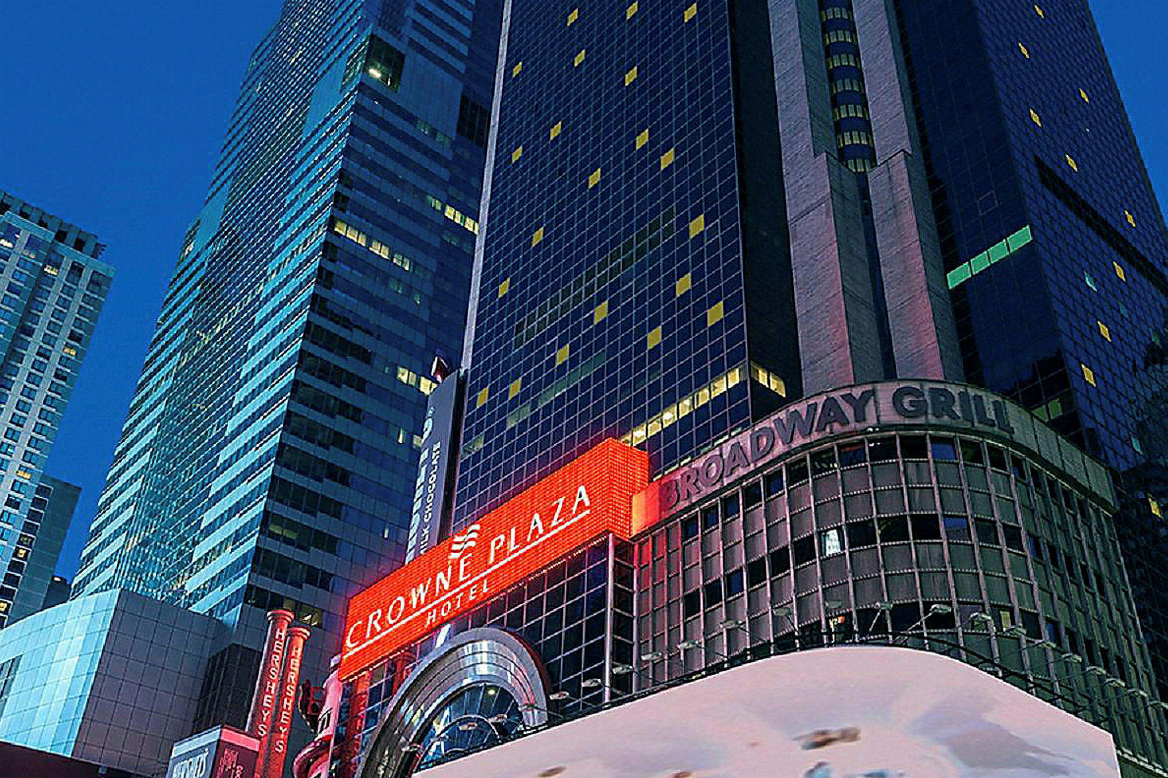 Et bilde av en høy bygning med neonskilt som viser "Crowne Plaza" og "Broadway Grill". (AI-generert tekst)