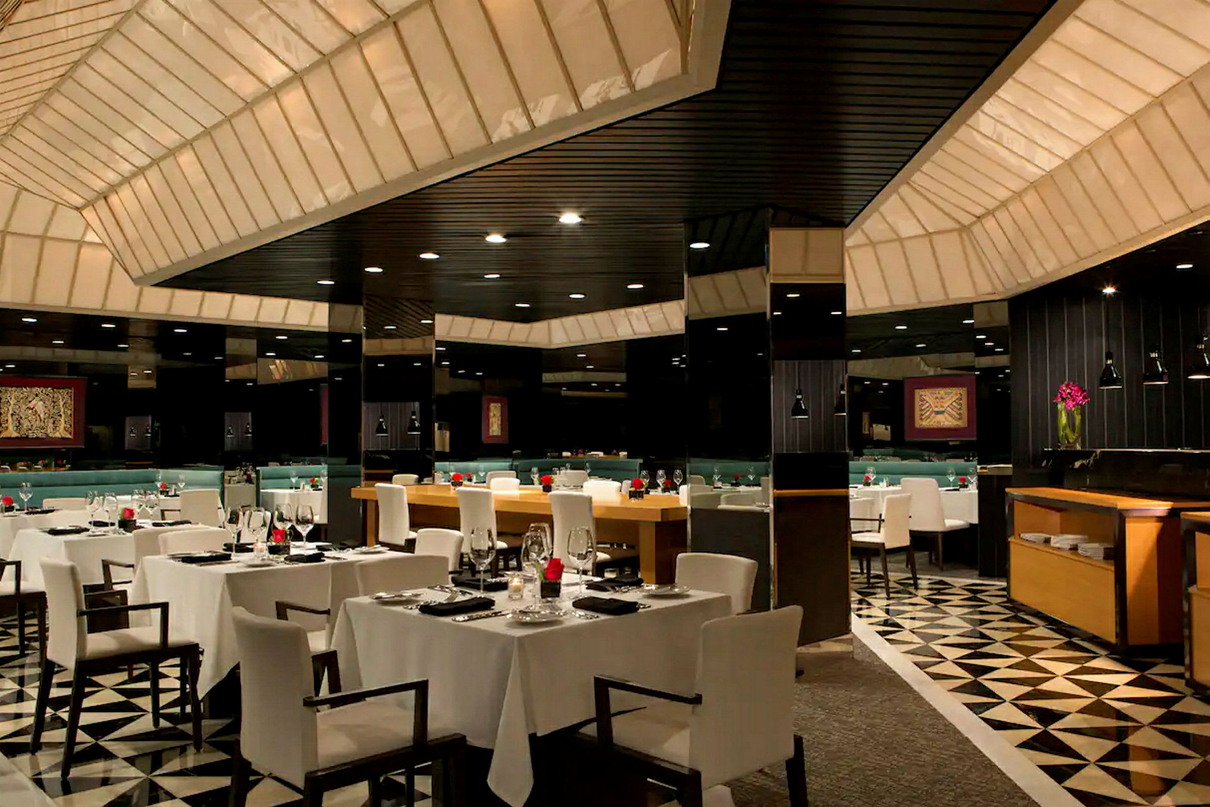 Bilde av en elegant restaurant med bord dekket med hvite duker og moderne sitteplasser. Rommet har en lavtakdesign med belysning og en stilig innredning. (AI-generert tekst)