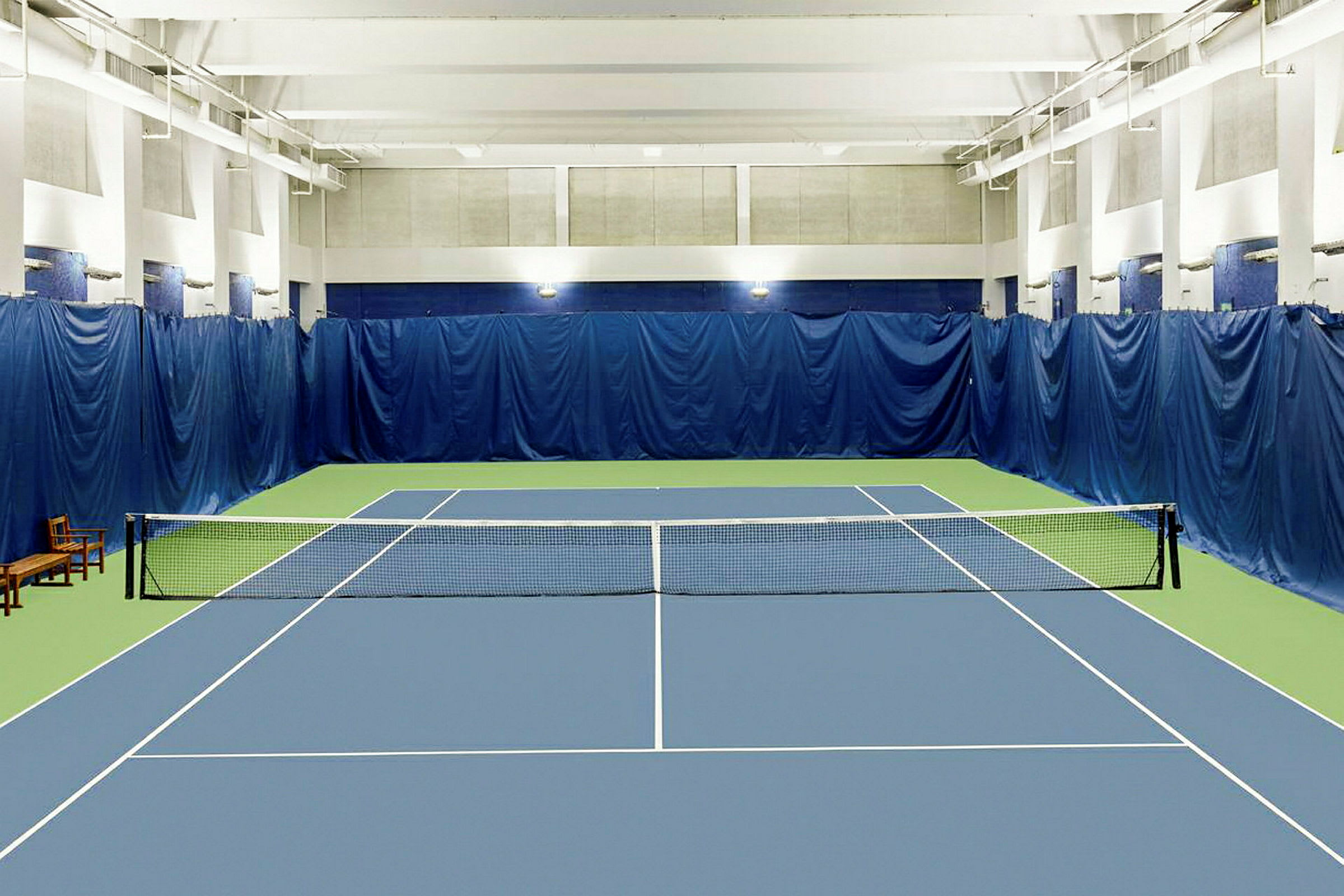 En innendørs tennisbane med blått og grønt underlag og et nett i midten. (AI-generert tekst)