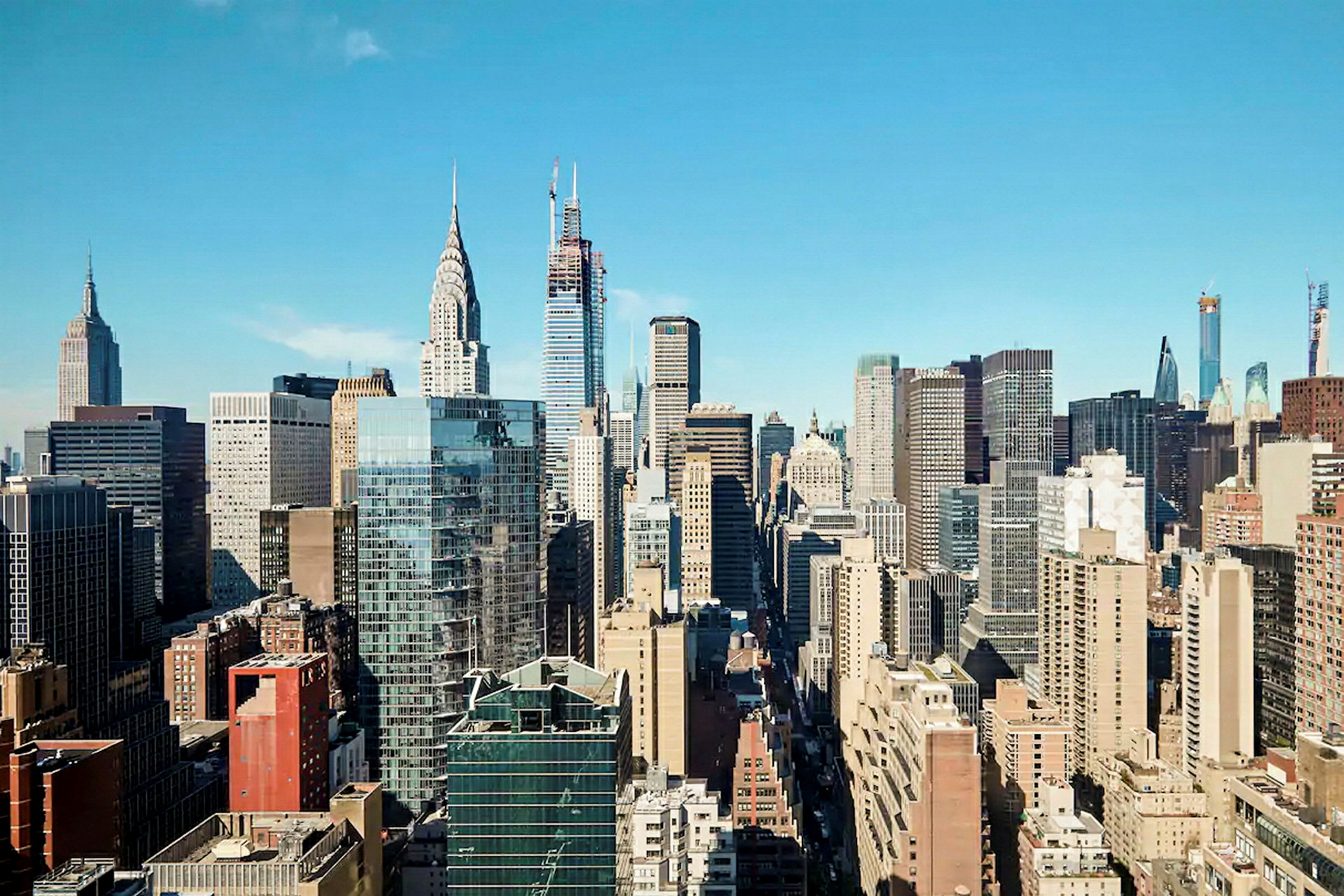 Utsikt over en by med mange skyskrapere og moderne arkitektur mot en blå himmel. (AI-generert tekst)