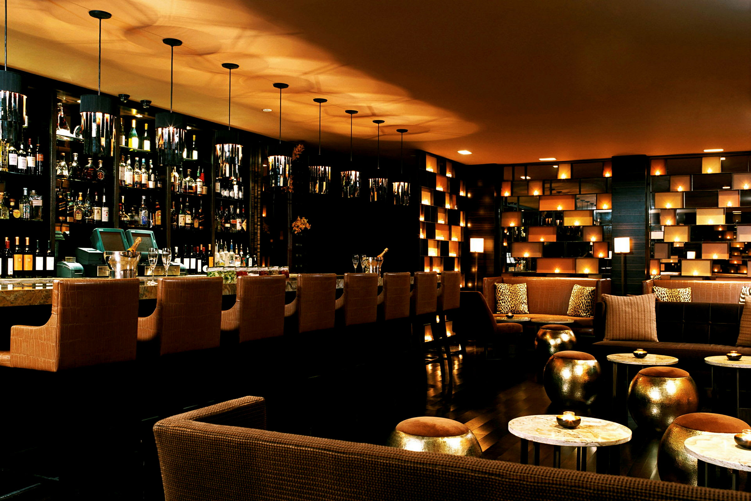 En elegant bar med høystoler ved bardisken, flasker i bakgrunnen, samt sofaer og bord med myk belysning. (AI-generert tekst)