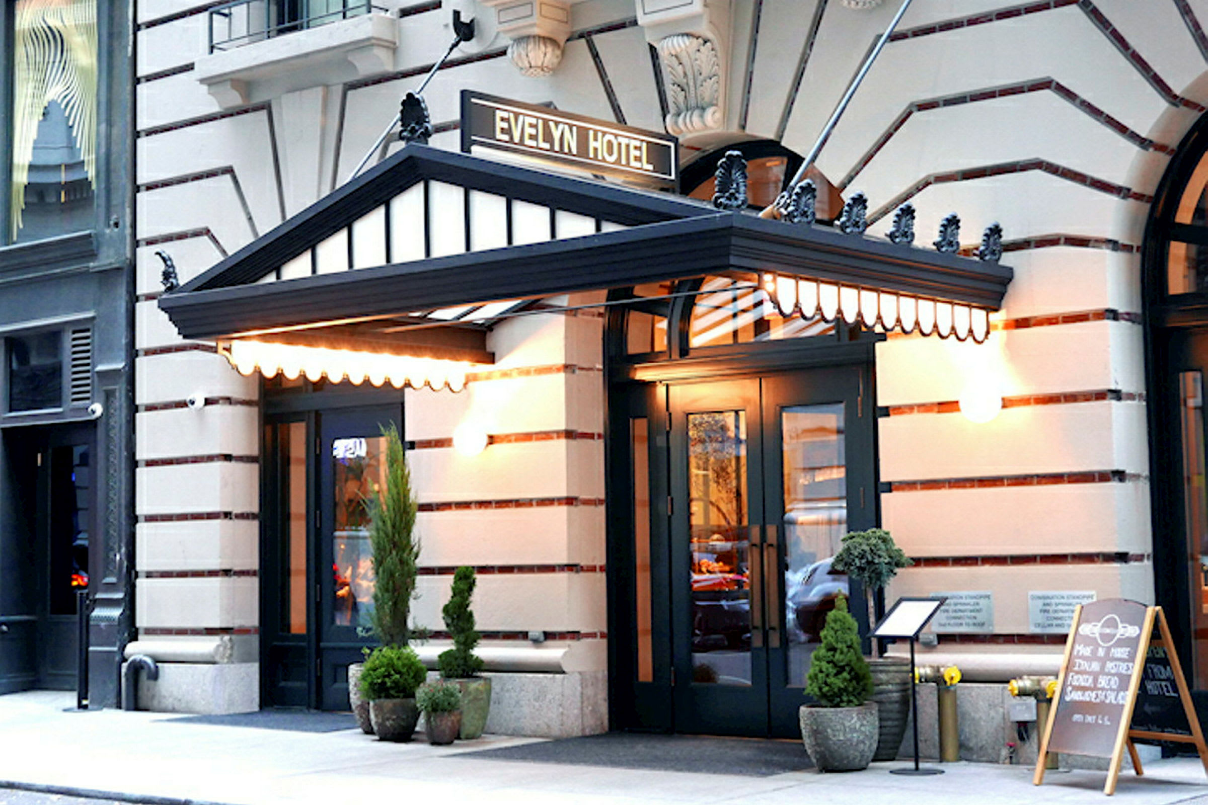 Hotellinngang med en svart baldakin og skiltet "Evelyn Hotel" over. Utenfor står plantekrukker og en meny på et stativ. (AI-generert tekst)