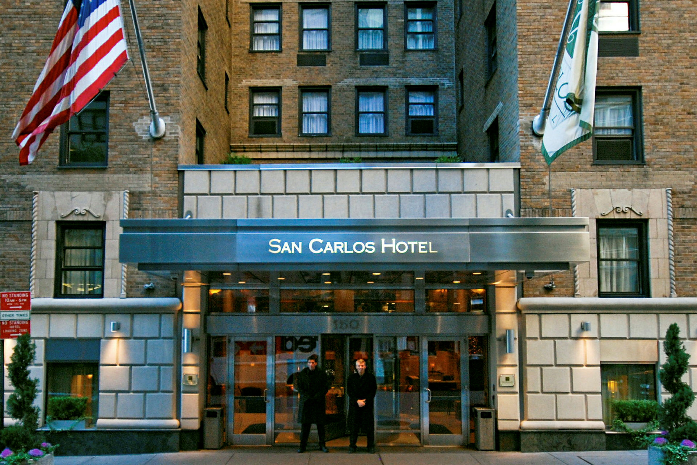 Inngangen til San Carlos Hotel, en bygningfasade med murstein og flagg. (AI-generert tekst)