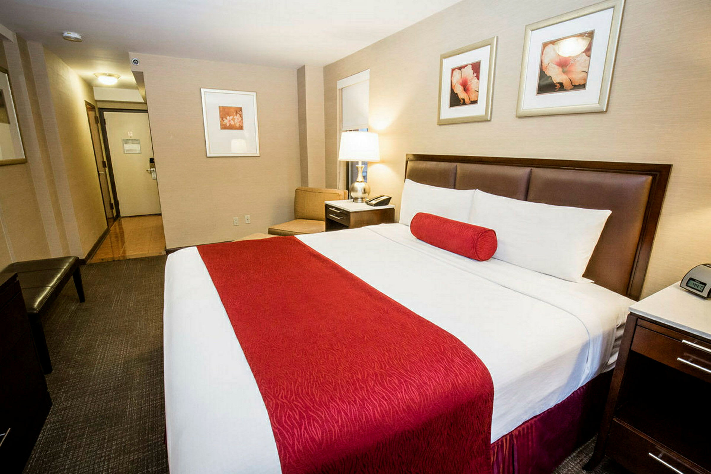 Hotellrom med en stor seng med røde detaljer. Skrivebord og lampearmatur i nærheten. (AI-generert tekst)