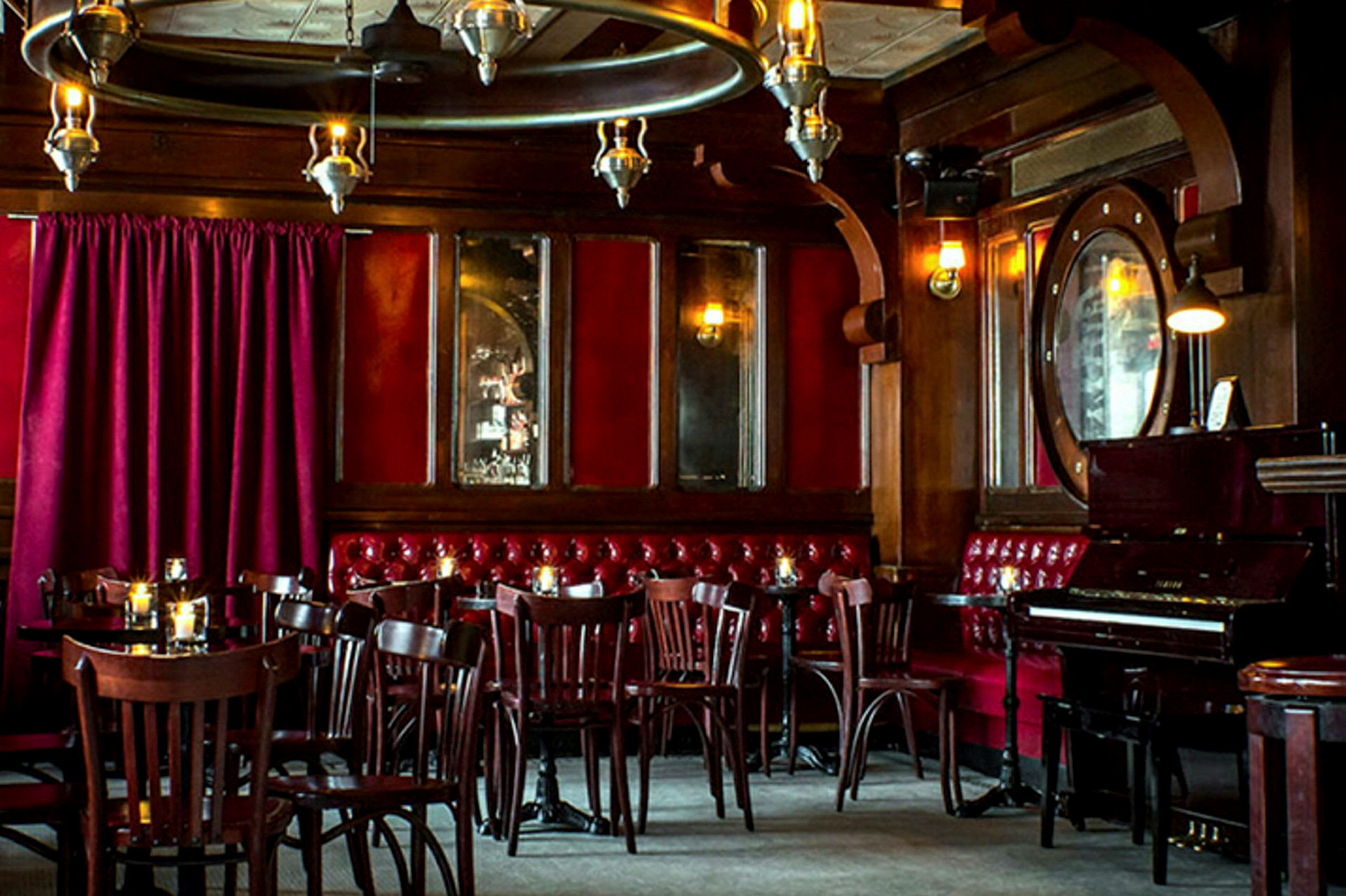 Et interiør av en restaurant eller bar med trepaneler, røde fløyelsgardiner og et piano. (AI-generert tekst)