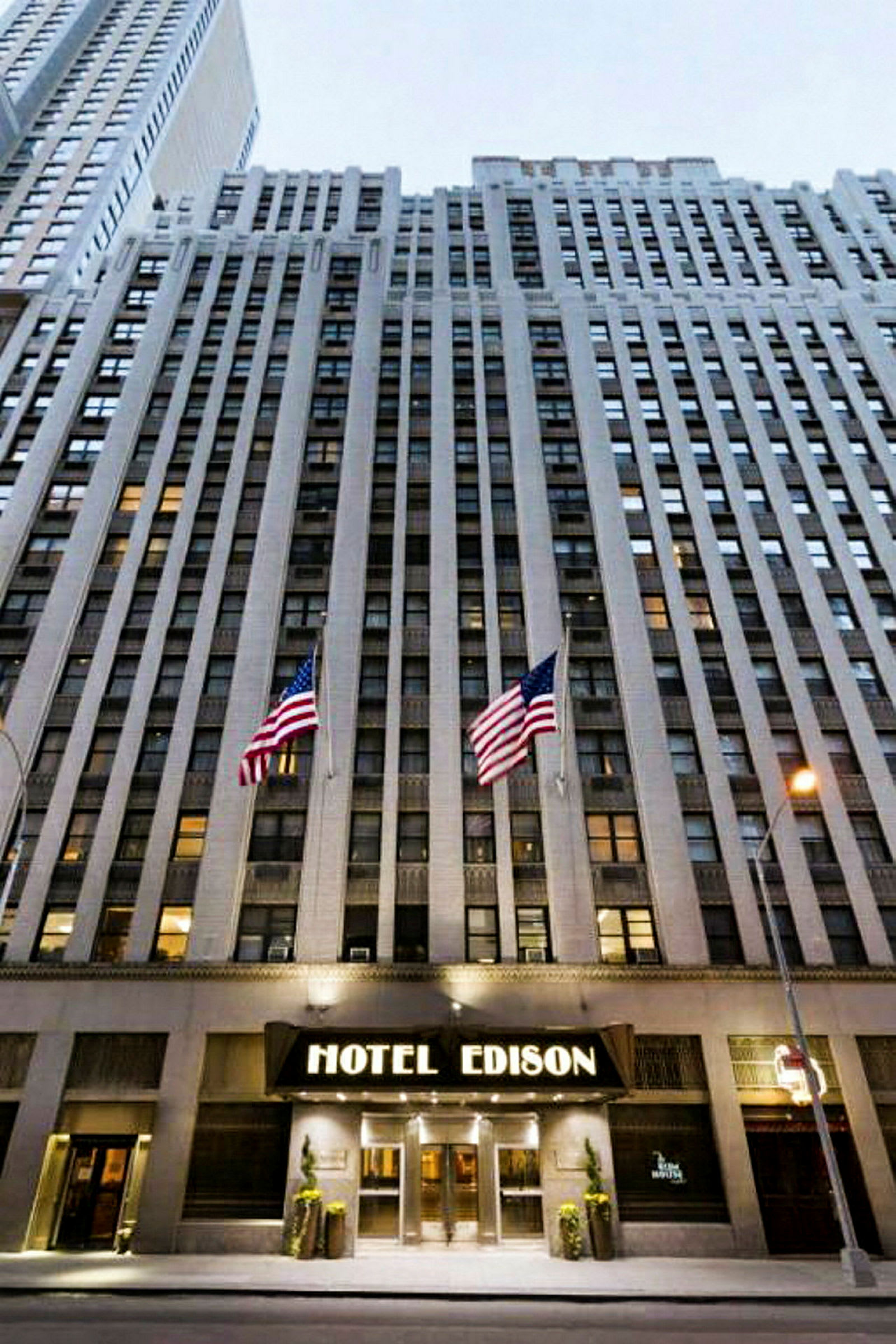 Utsikt mot en høy bygning med inngangen merket "Hotel Edison" og to amerikanske flagg foran. (AI-generert tekst)