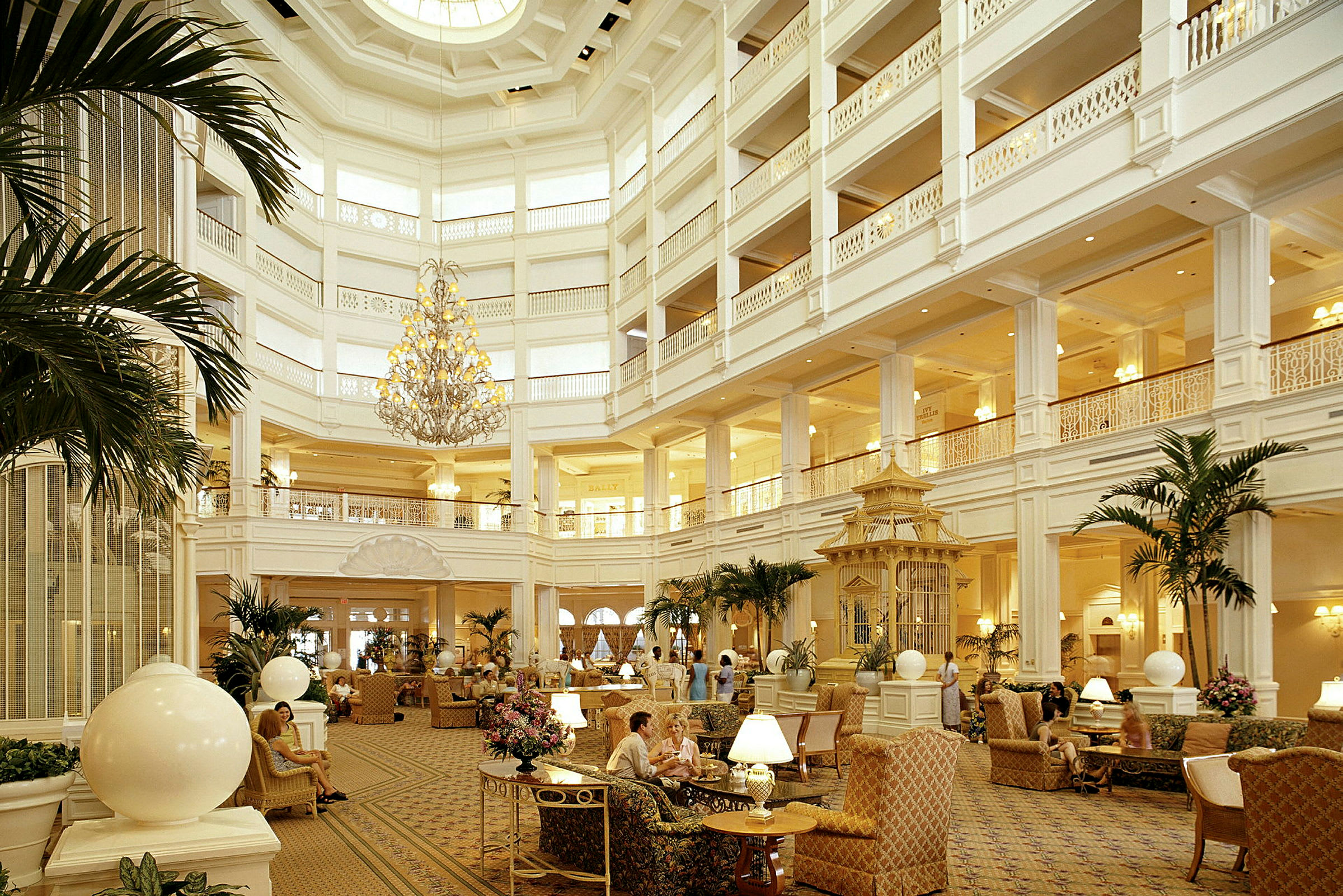 En stor og elegant hotellobby med høyt tak, en storslått lysekrone, komfortable sitteplasser og planter som dekorasjon. (AI-generert tekst)