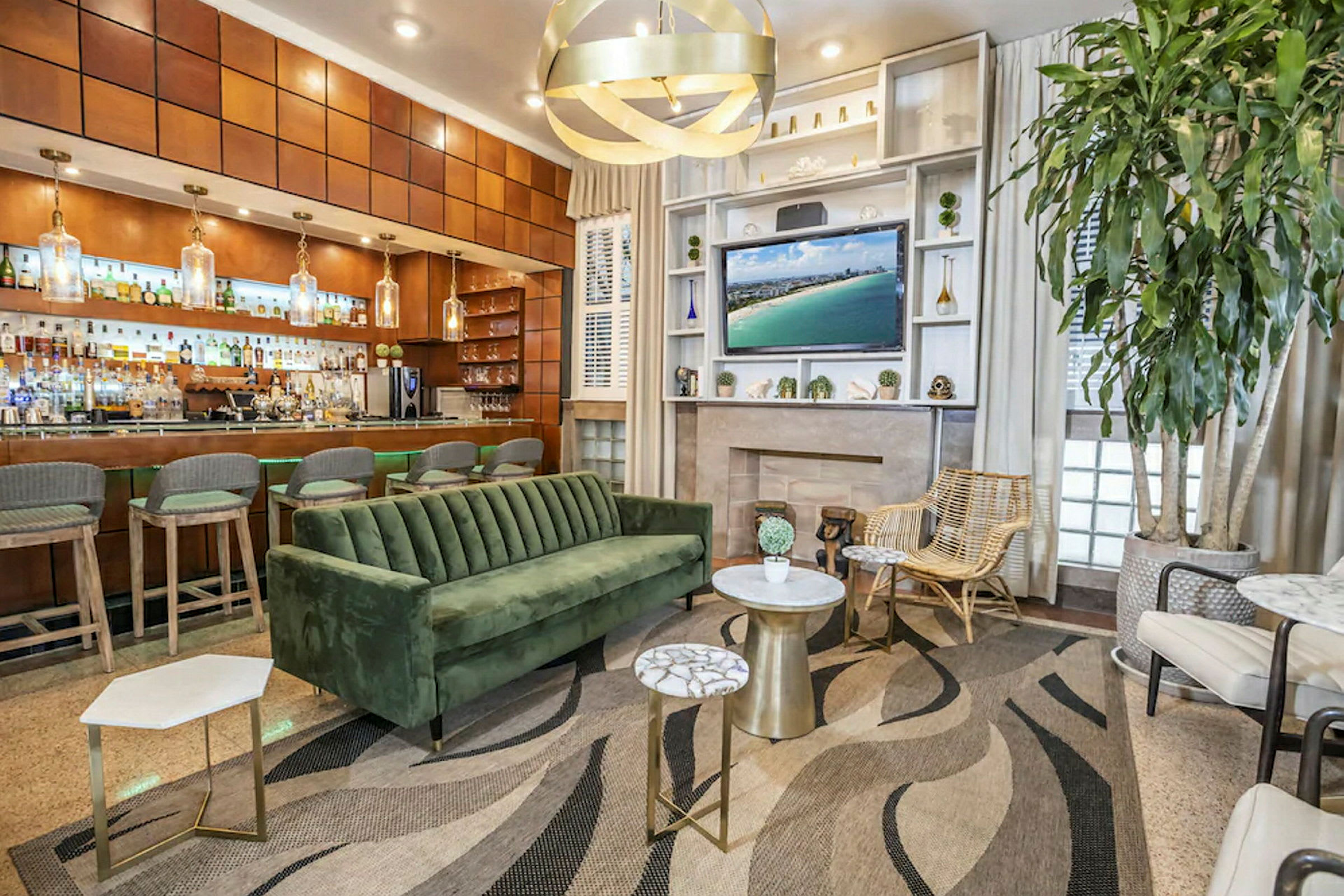 Et moderne loungeområde med en grønn fløyelssovesofa, flere små bord, en stor plante og en bar i bakgrunnen. (AI-generert tekst)