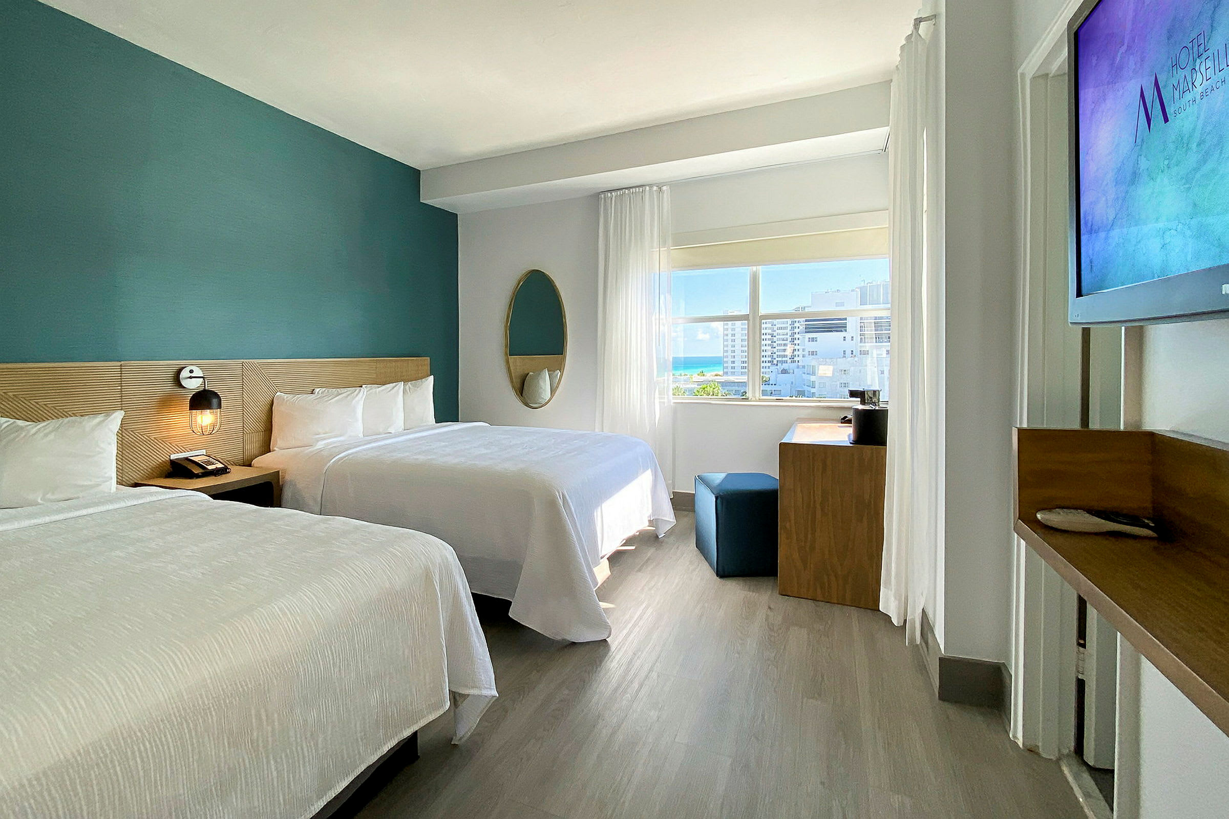 Et moderne hotellrom med to dobbeltsenger, et skrivebord og et stort vindu som slipper inn naturlig lys. (AI-generert tekst)