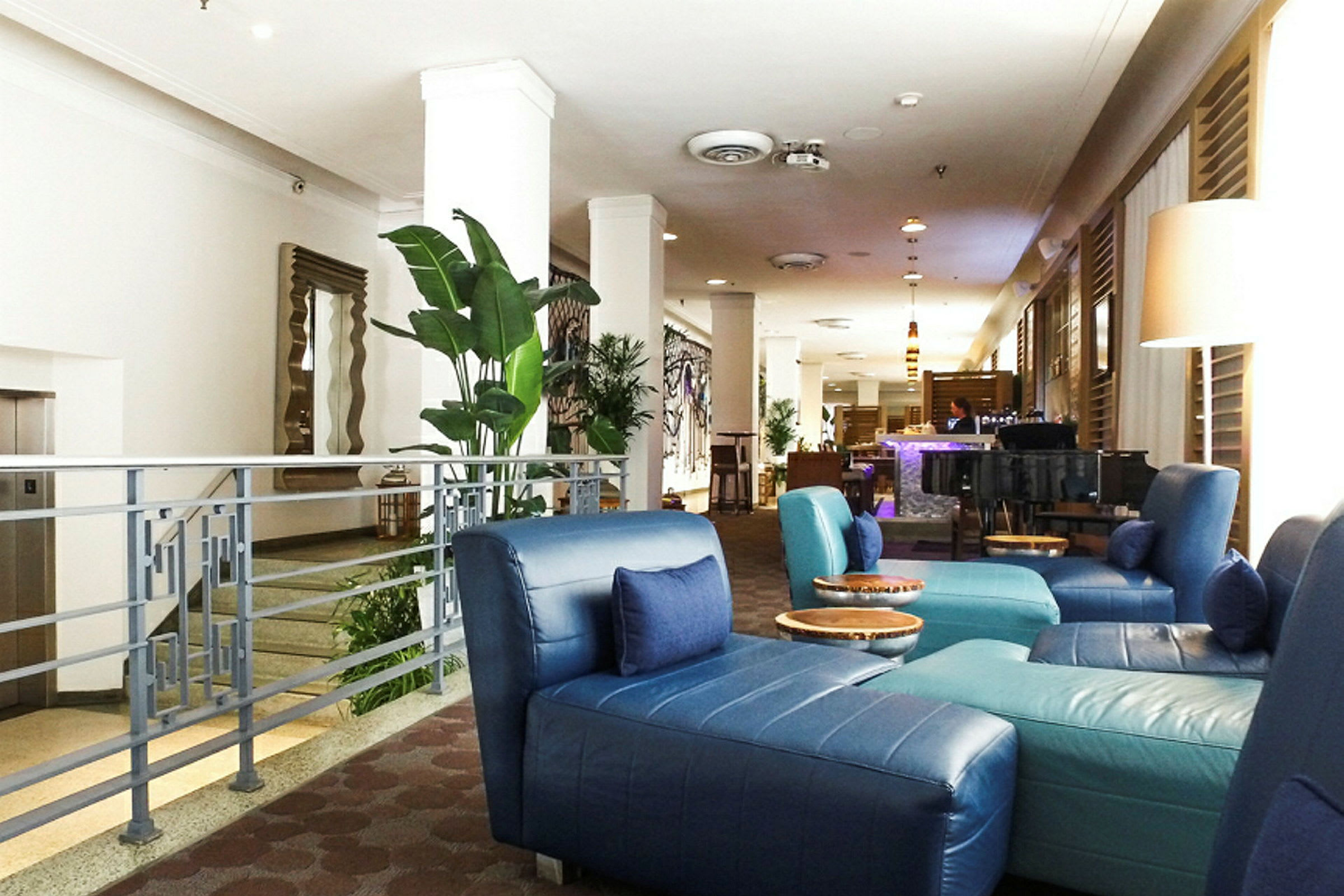 Bilde av en hotellobby med blå sittemøbler, grønne planter og en bar i bakgrunnen. (AI-generert tekst)