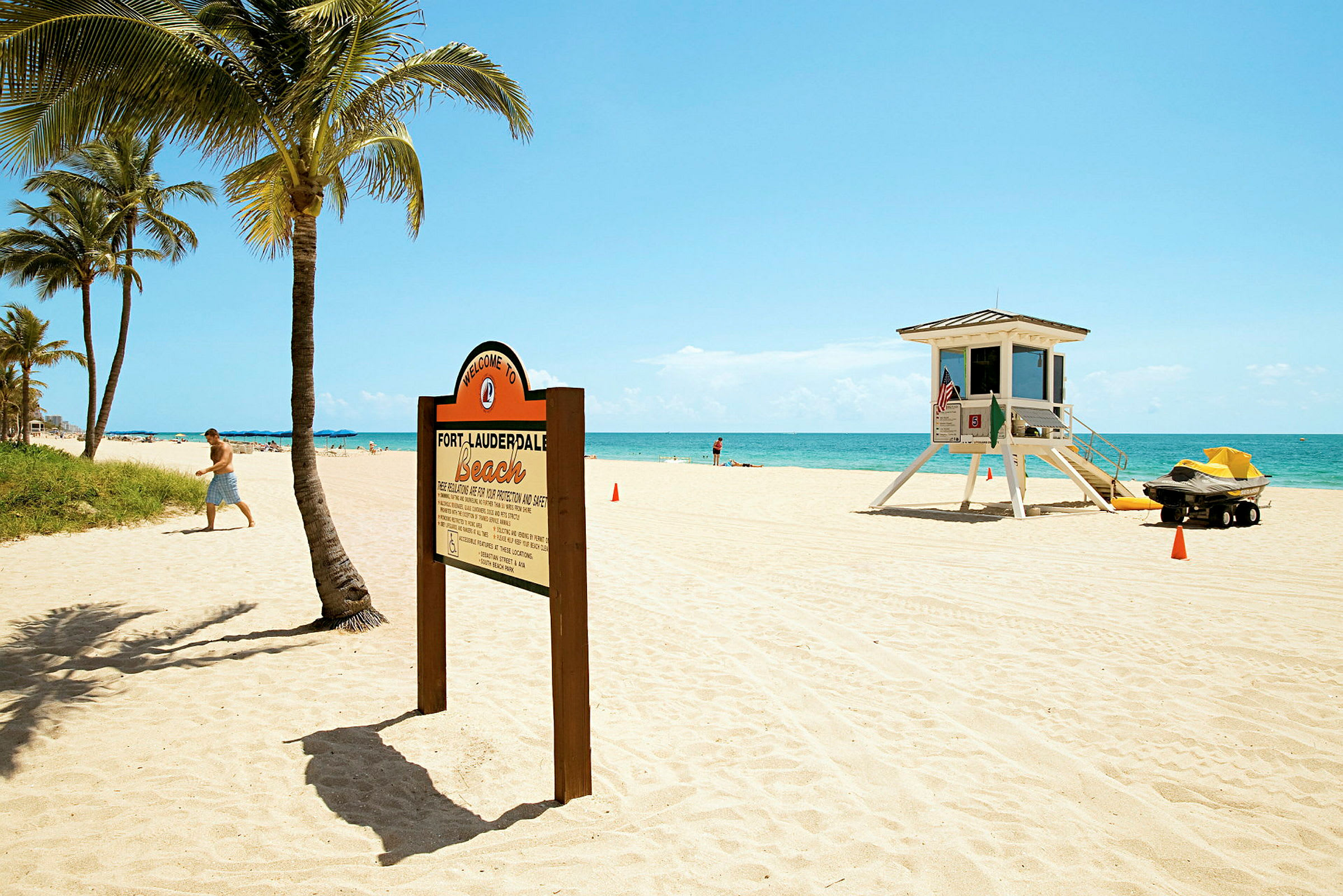 En sandstrand med palmer, et skilt som ønsker velkommen til Fort Lauderdale Beach og et livreddertårn. (AI-generert tekst)