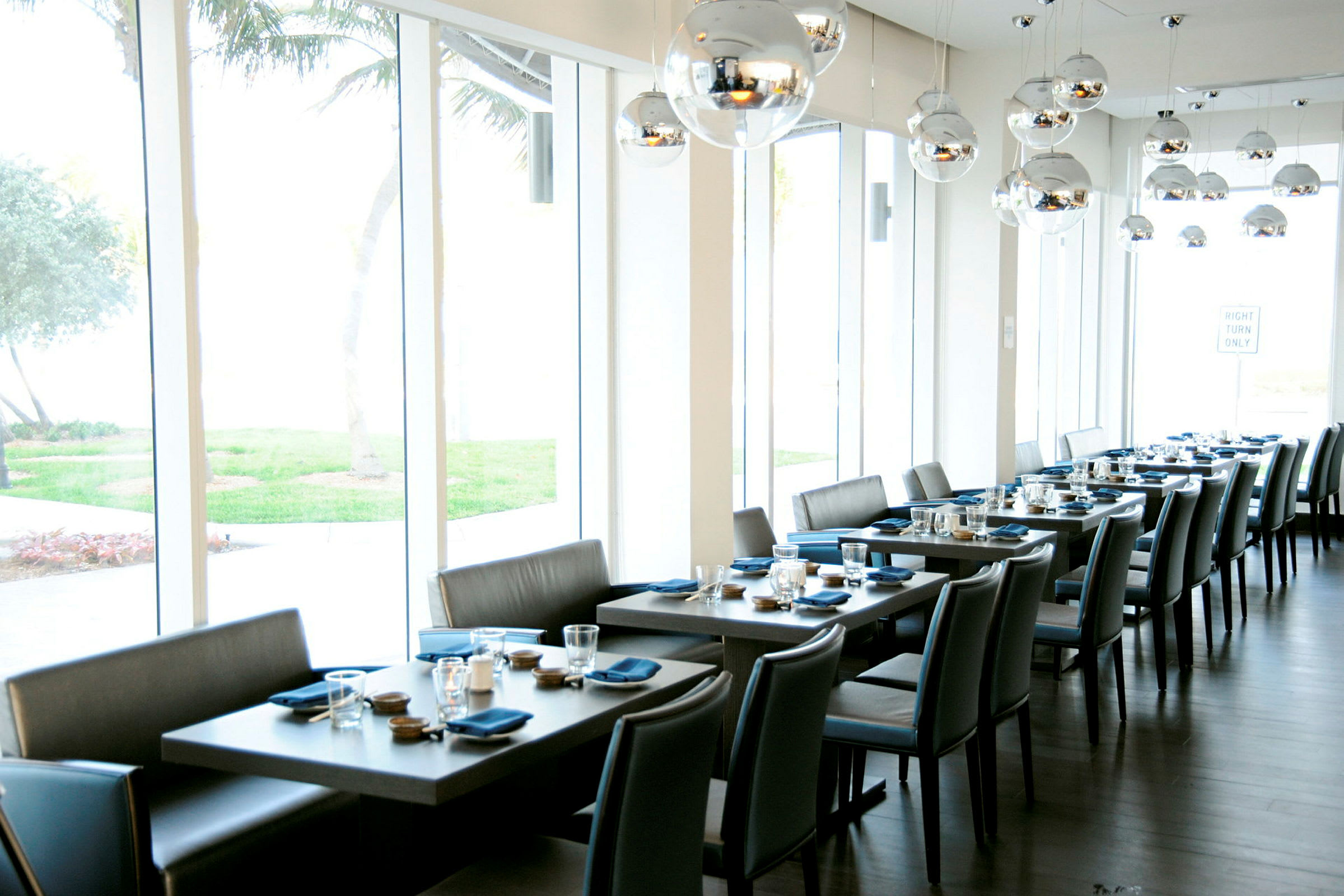 En moderne restaurant med flere dekkede bord, utsikt mot grøntområder og store vinduer. (AI-generert tekst)