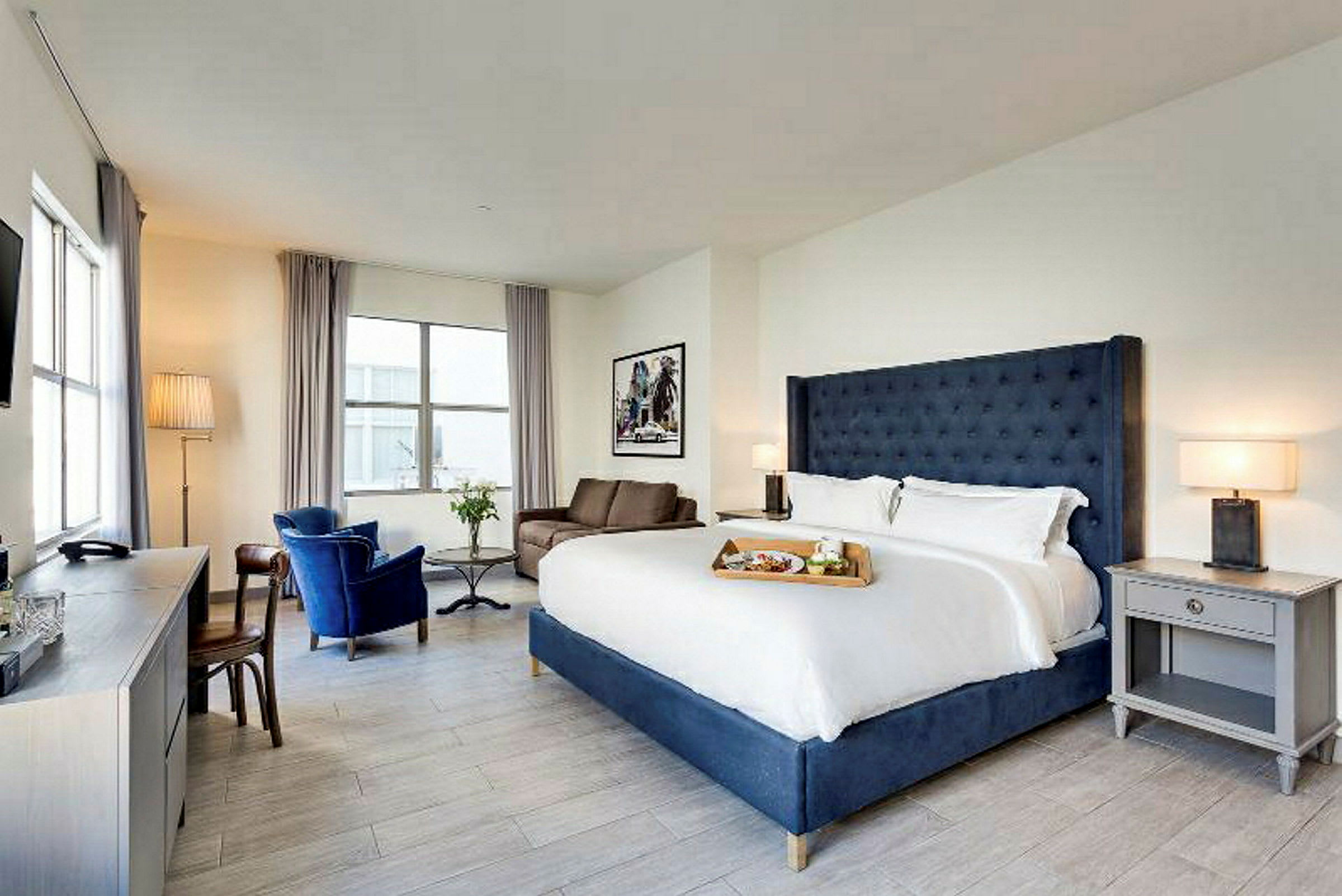 Et lyst hotellrom med stor dobbeltseng, lenestoler og et skrivebord. (AI-generert tekst)