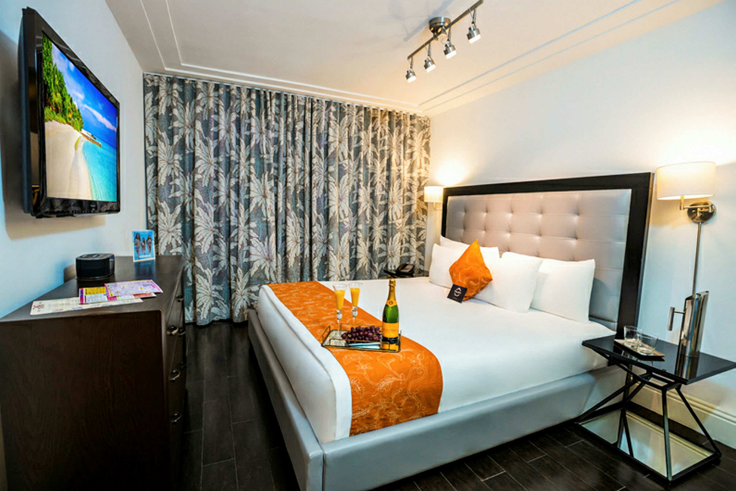 Et hotellrom med en dobbeltseng i hvitt og oransje, et bord ved siden av og en TV på veggen. (AI-generert tekst)