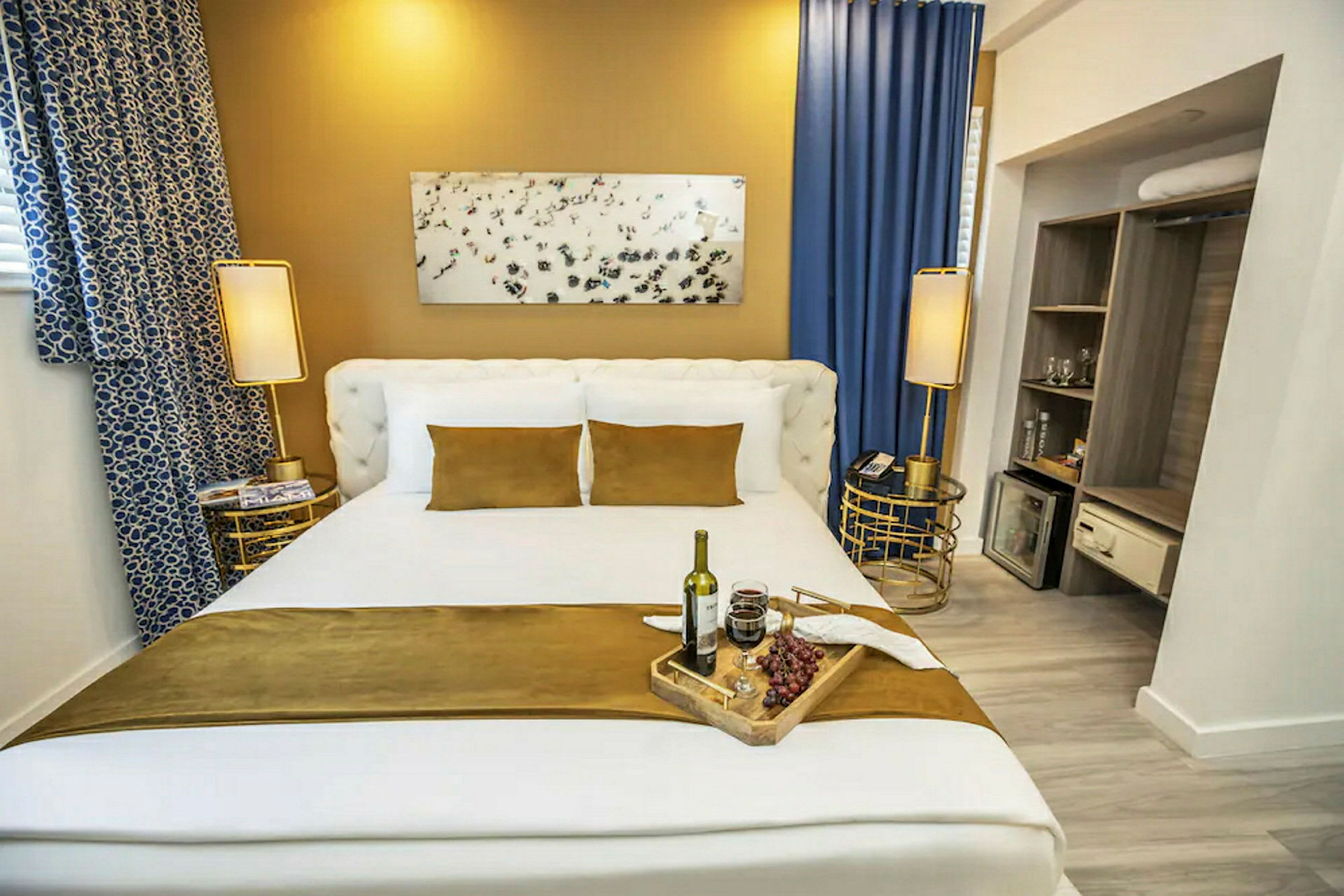 Et hotellrom med en stor seng oppredd med hvite og gyllenbrune tekstiler. Detaljer inkluderer nattbord og dekorasjoner. (AI-generert tekst)
