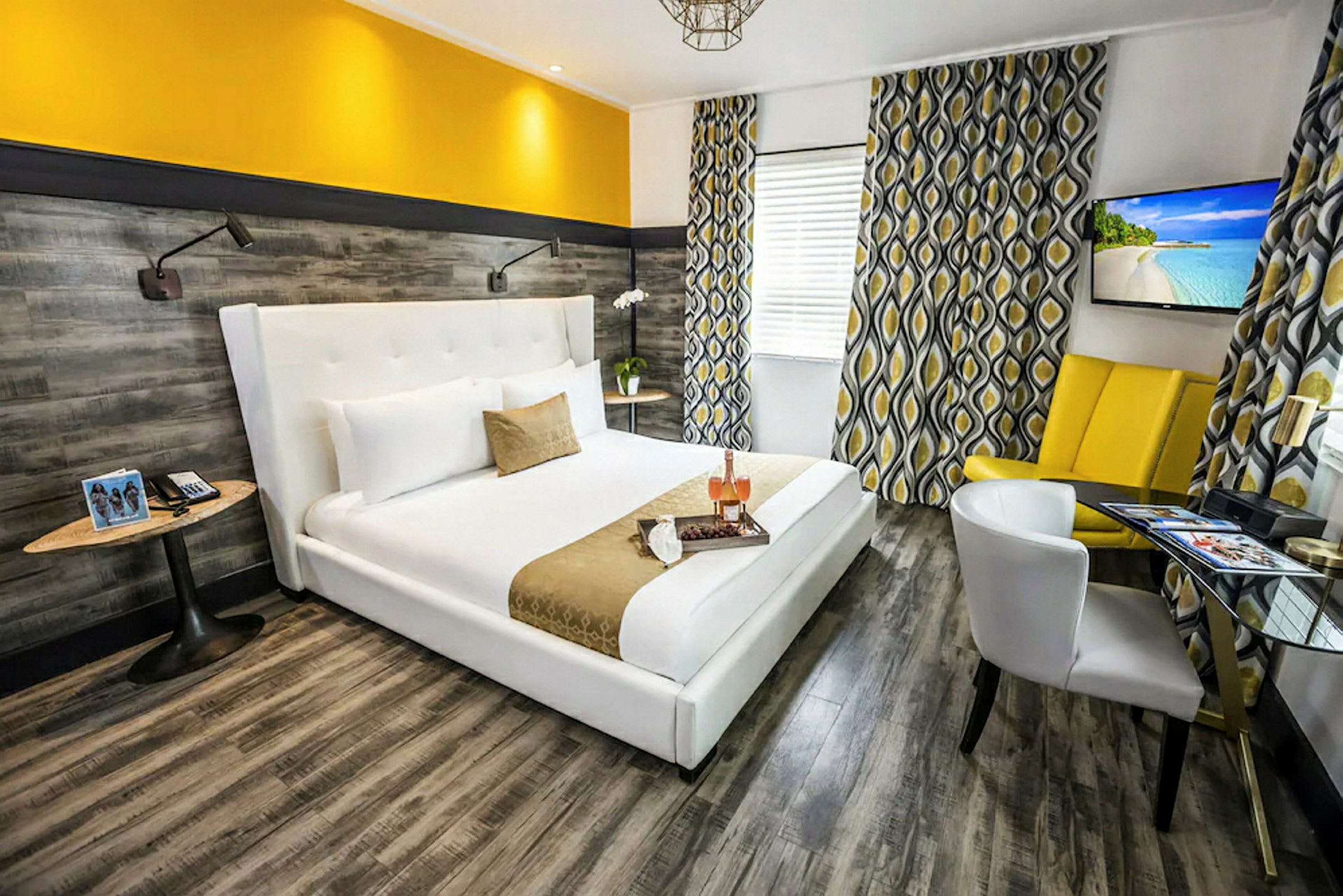 Et moderne hotellrom med en bred, hvit seng og gule dekorasjonsdetaljer. Veggene har en tremønstret finish, og vinduene er dekorert med mønstrede gardiner. (AI-generert tekst)