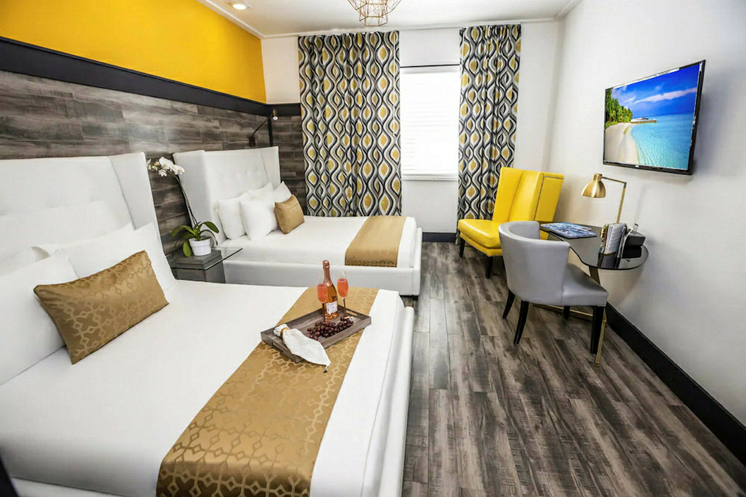 Et hotellrom med to hvite senger, gul og grå innredning samt en TV på veggen. (AI-generert tekst)
