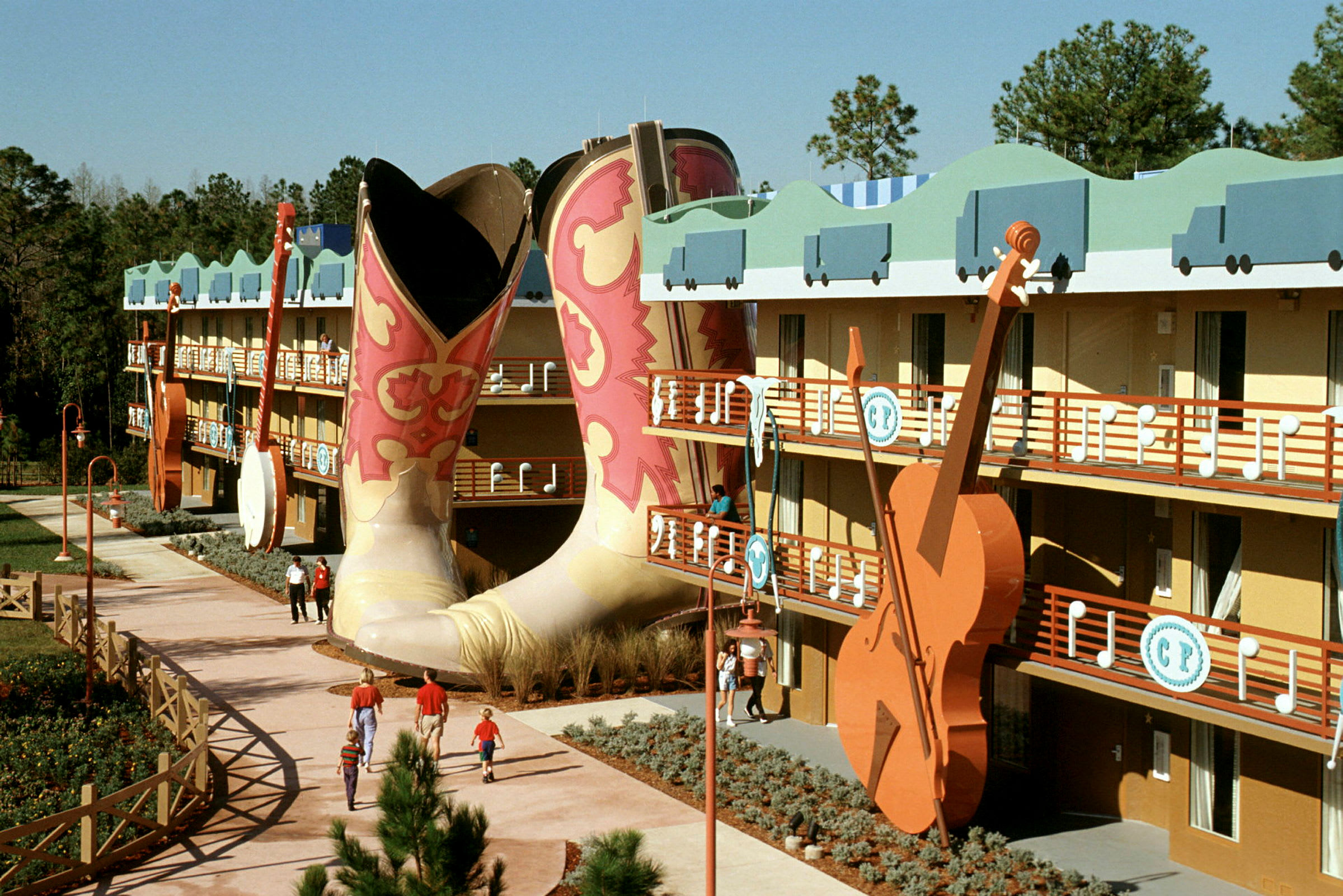 Et fargerikt hotellkompleks med store cowboyboots og en gitar i dekor. Folk går på gangveien. (AI-generert tekst)