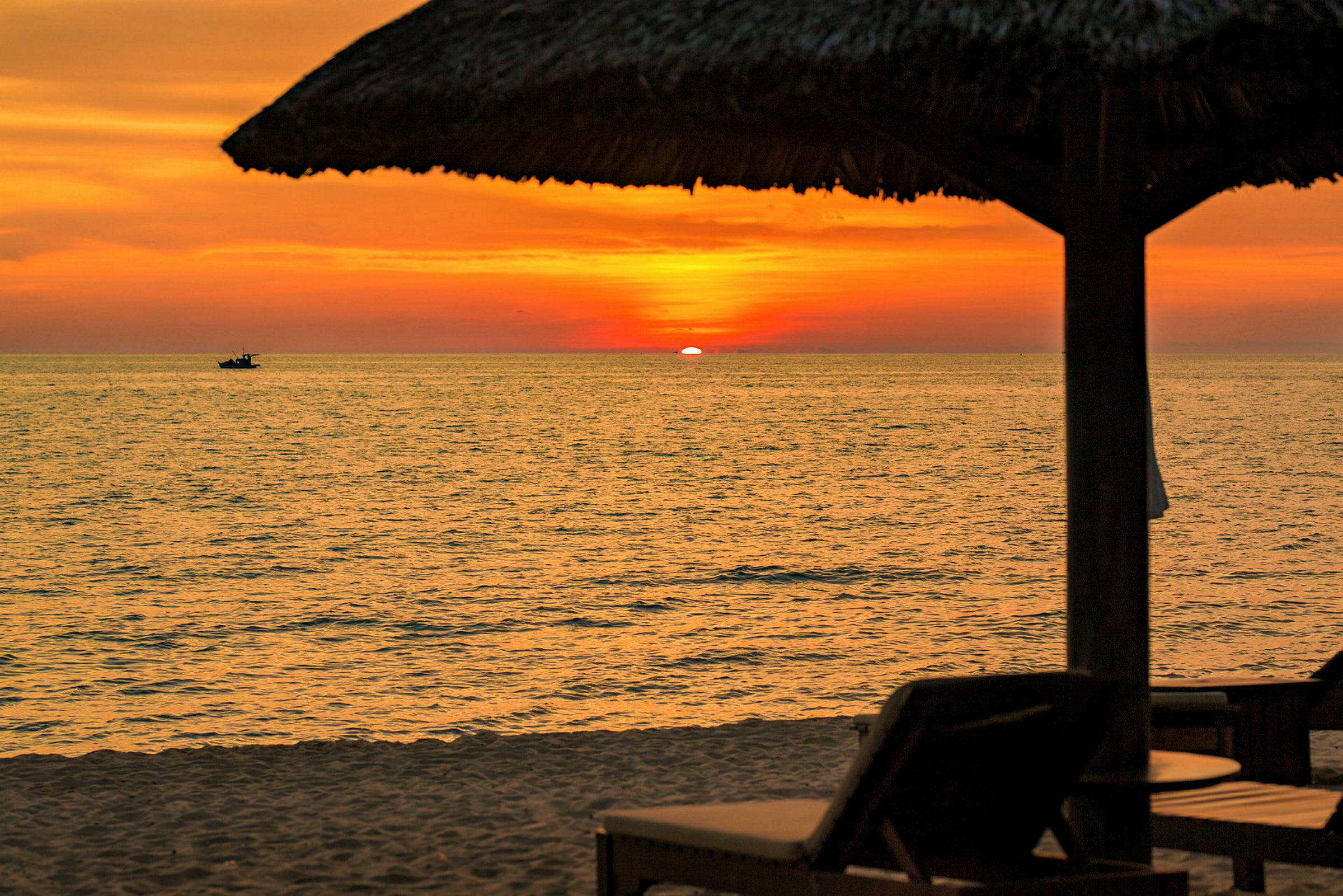 Solnedgang over havet med en strand i forgrunnen og silhuetter av solsenger og parasoller. (AI-generert tekst)