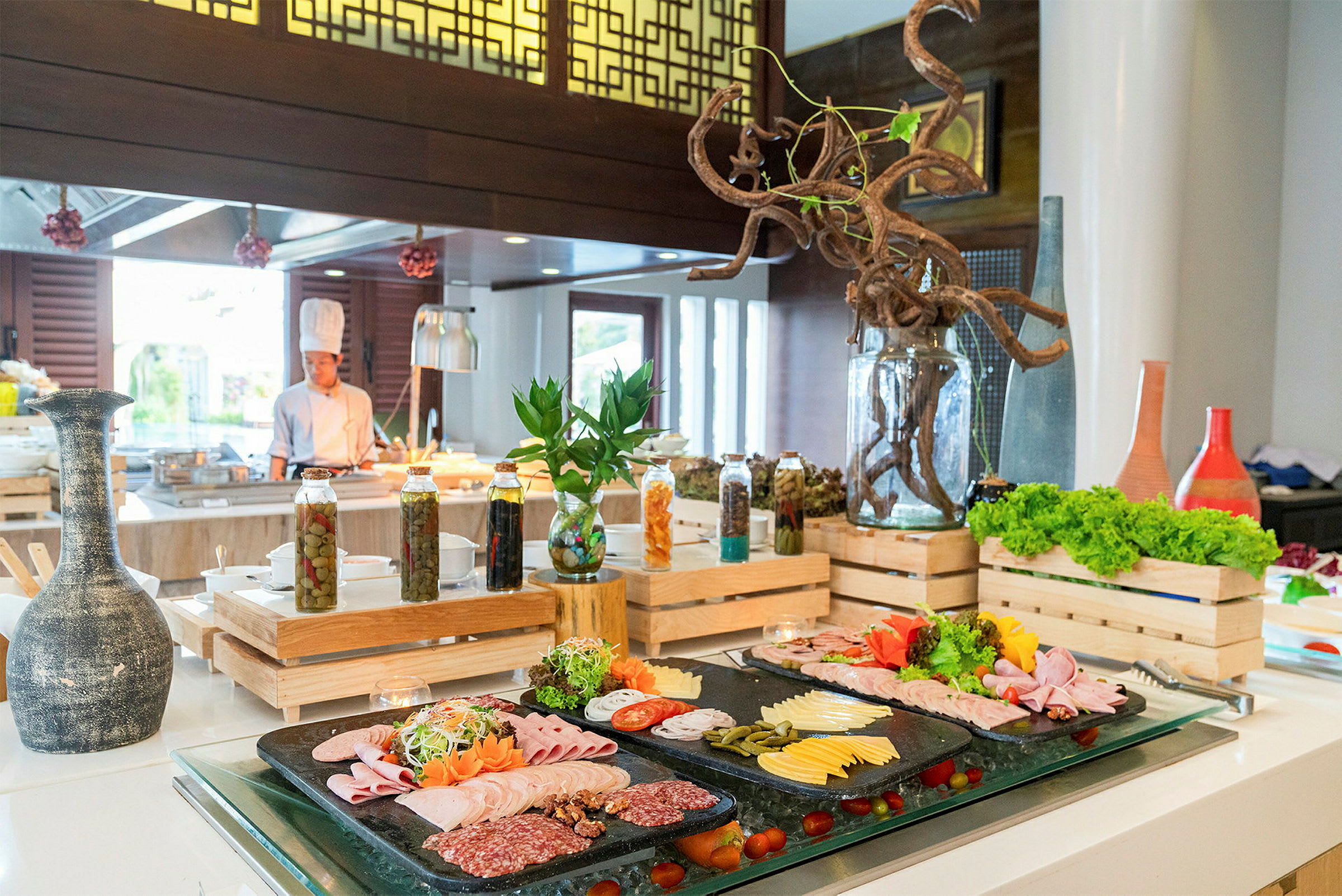 Bilde av en buffet med kaldskjæringer, oster og salater, omgitt av dekorative detaljer og serveringsutstyr. En kokk vises i bakgrunnen. (AI-generert tekst)