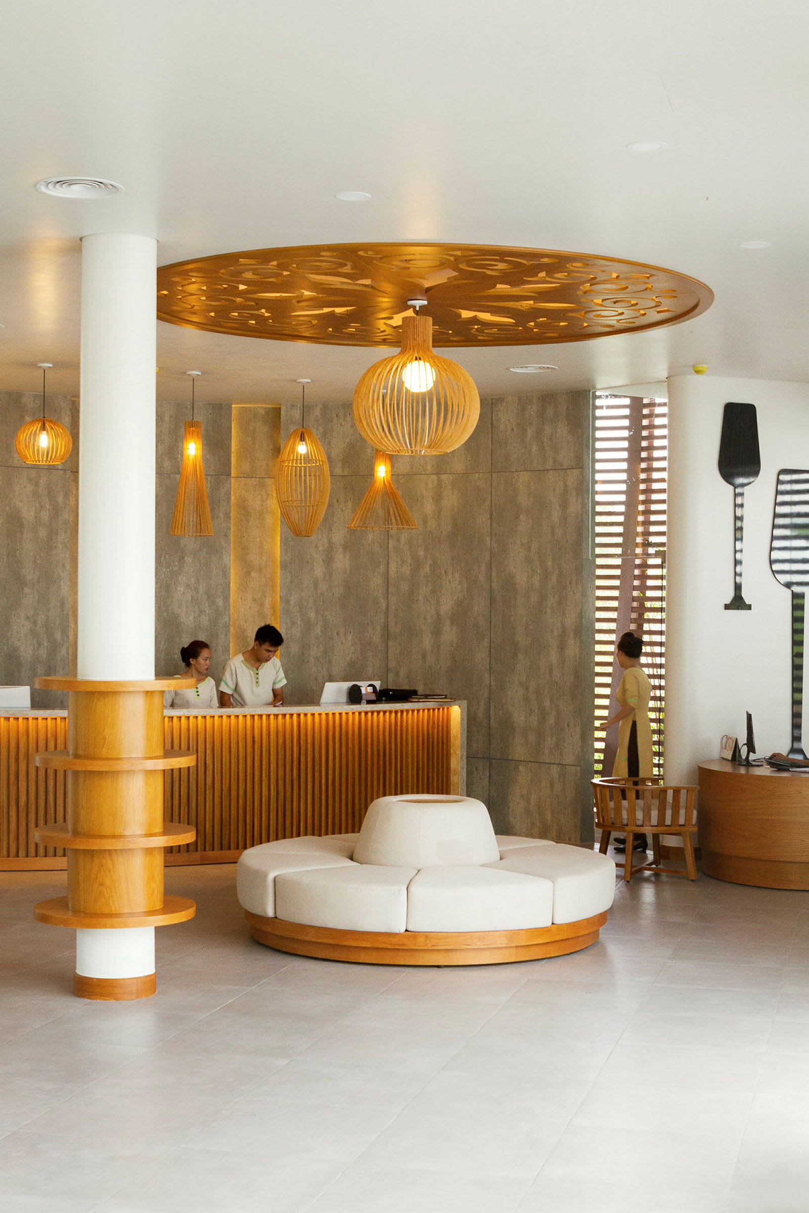 En hotellresepsjon med moderne og elegant interiør. Det er en disk med ansatte, en rund sitteenhet midt i rommet og dekorative lamper i taket. (AI-generert tekst)