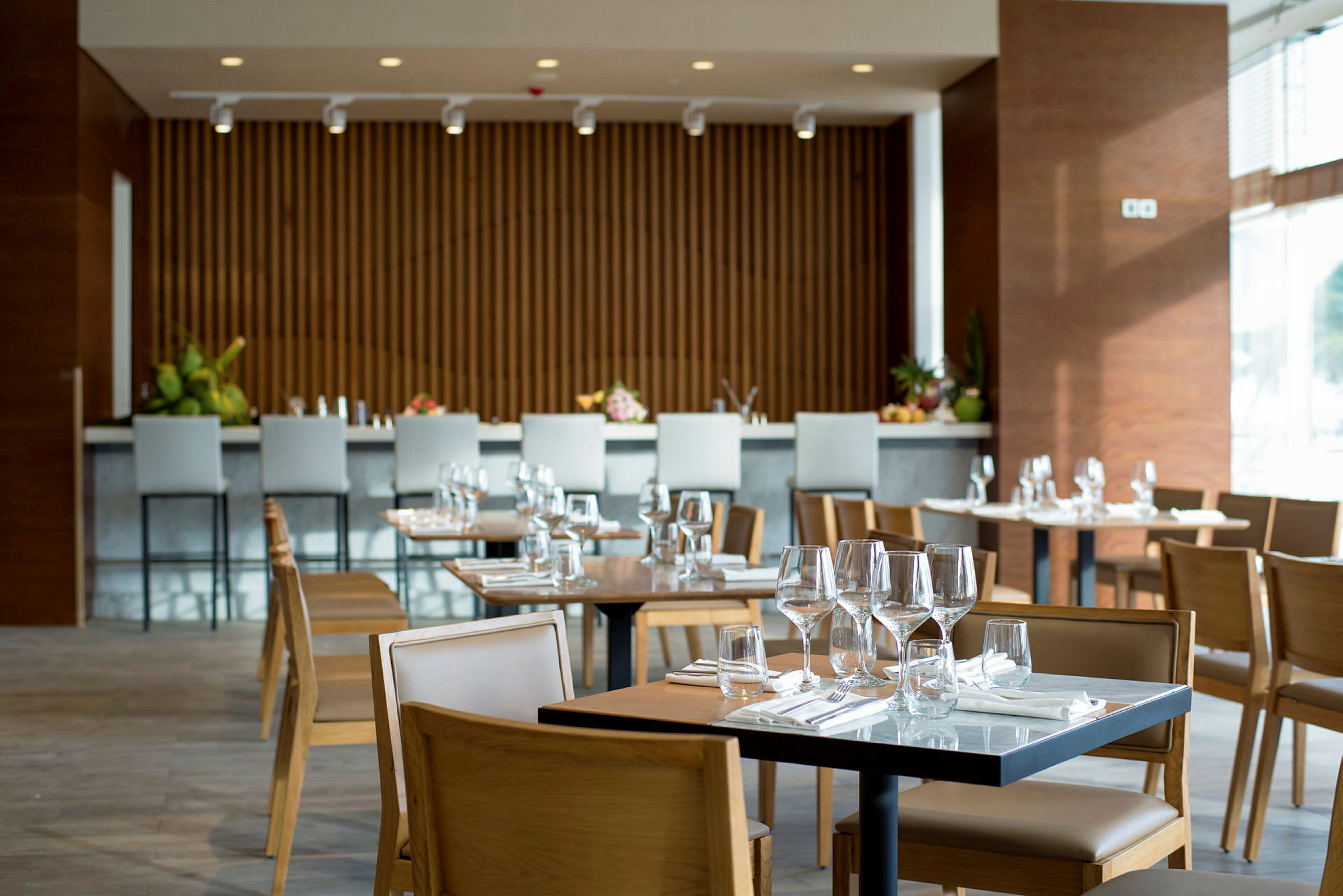 Et moderne restaurantområde med trebord og stoler, dekket med glass og bestikk. (AI-generert tekst)