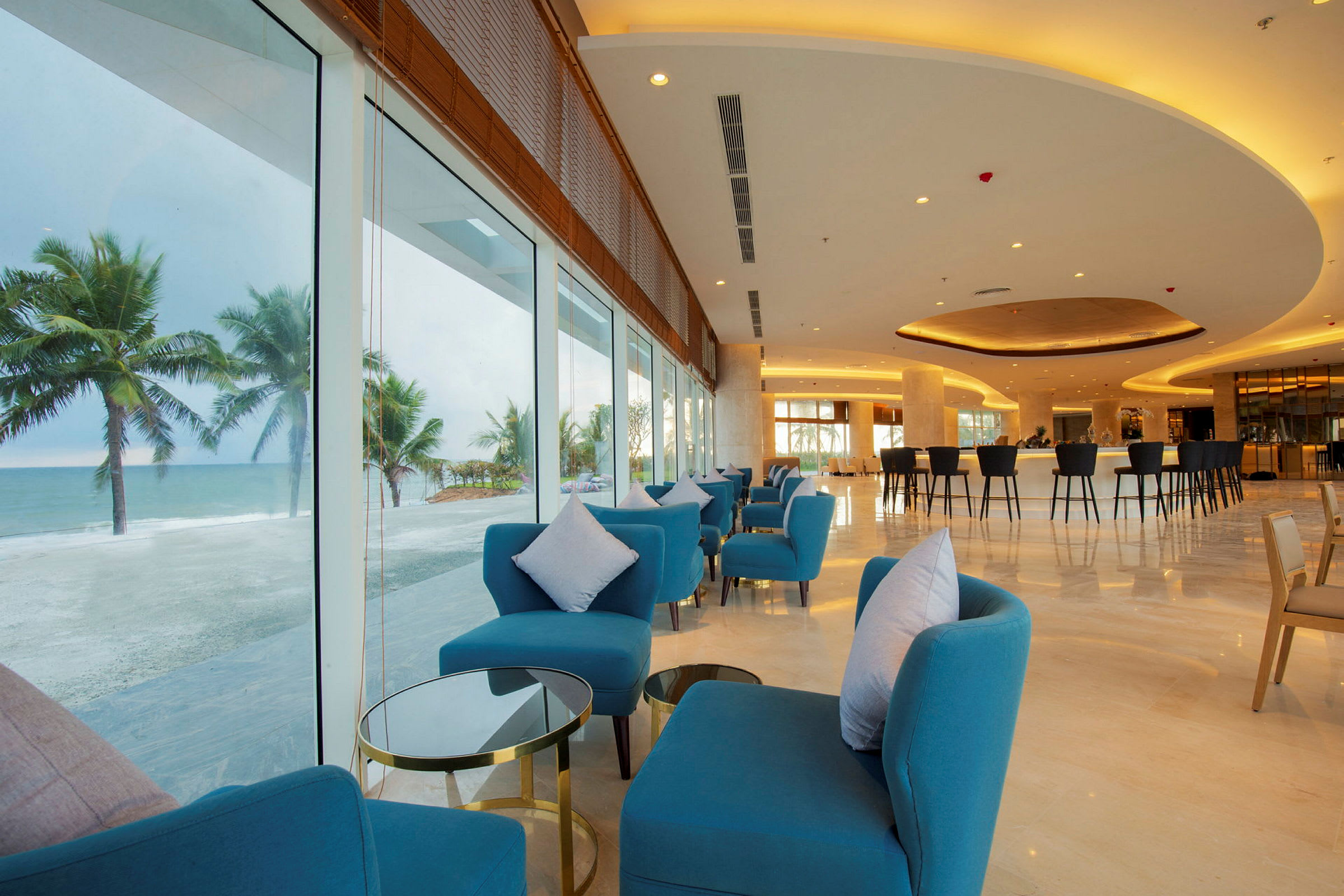 En hotellobby med sittegrupper og bord, vinduer som vender mot stranden og havet. (AI-generert tekst)