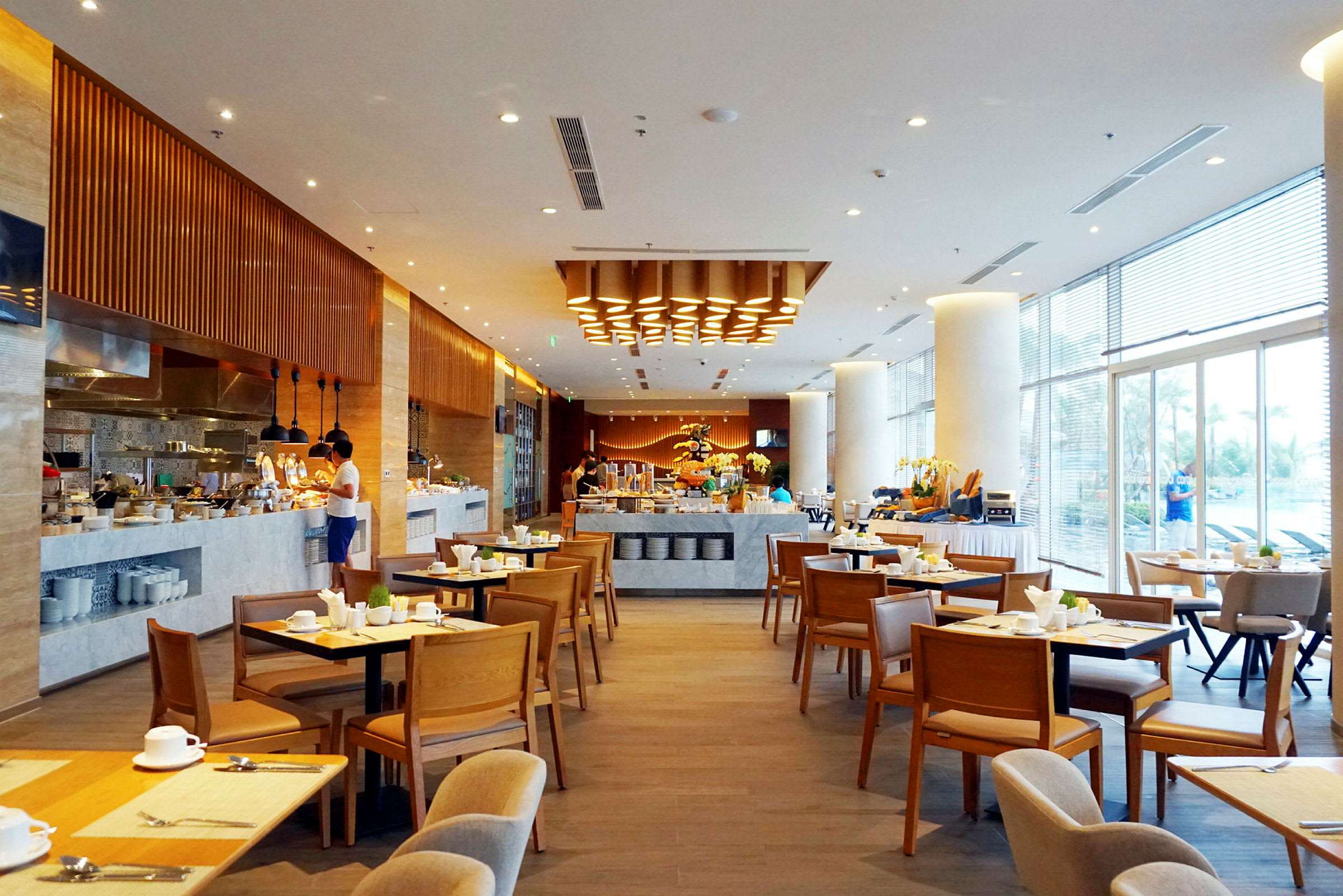 En romslig restaurant med bord og stoler, en bufféstasjon og moderne belysning. (AI-generert tekst)