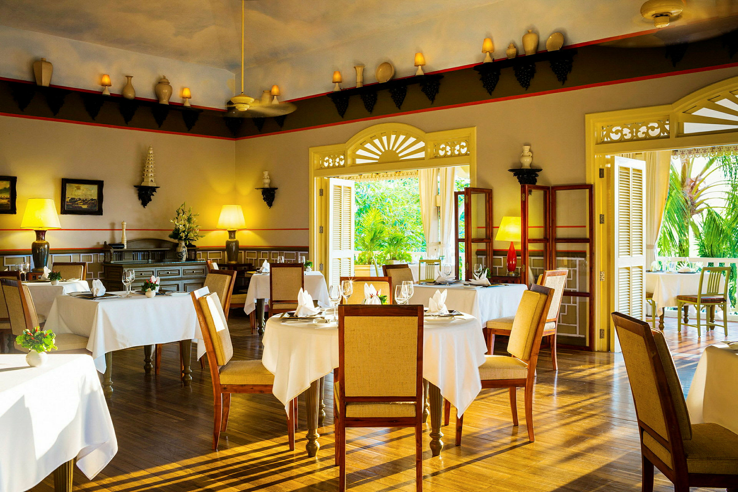 Interiør av en elegant restaurant med bord dekket med hvite duker, trestoler og dekorative elementer på veggene. (AI-generert tekst)