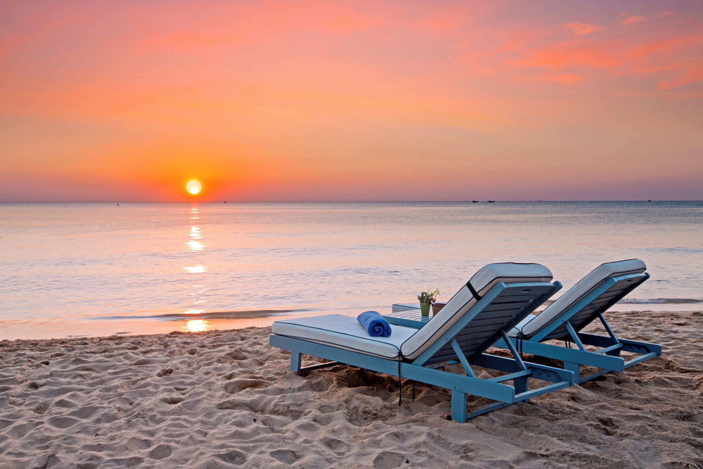 To solsenger står på sandstranden ved havet, med en solnedgang i bakgrunnen. (AI-generert tekst)