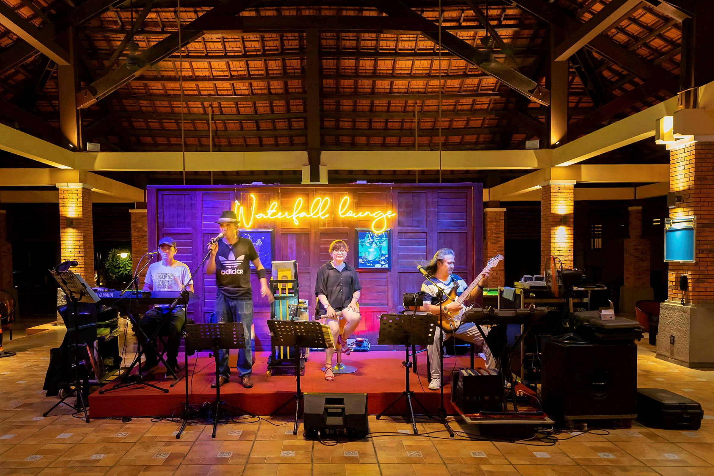 En gruppe musikere opptrer på en scene innendørs med et skilt som lyser "Waterfall lounge" i bakgrunnen. (AI-generert tekst)
