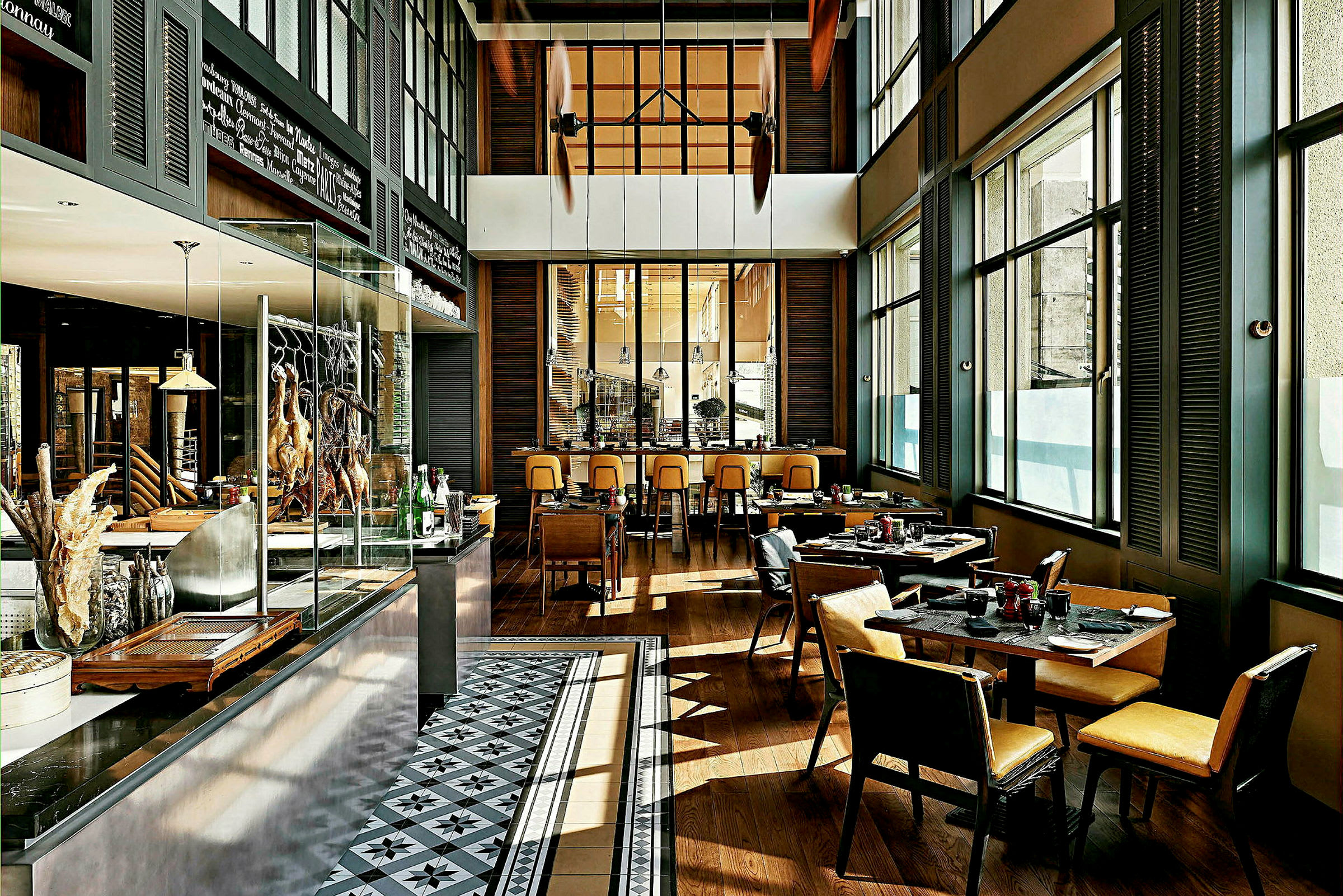 Interiør av en moderne restaurant med bord og stoler, store vinduer og et åpent kjøkkenområde. (AI-generert tekst)
