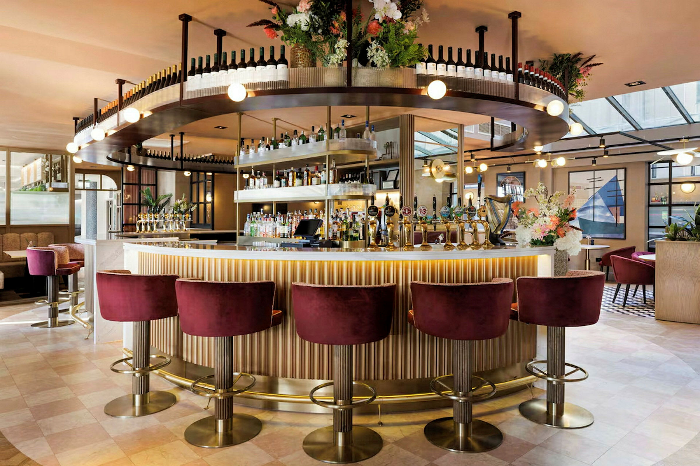 En elegant bar med vinflasker på hyller, blomsterarrangement og sitteplasser med røde fløyelsstoler. (AI-generert tekst)