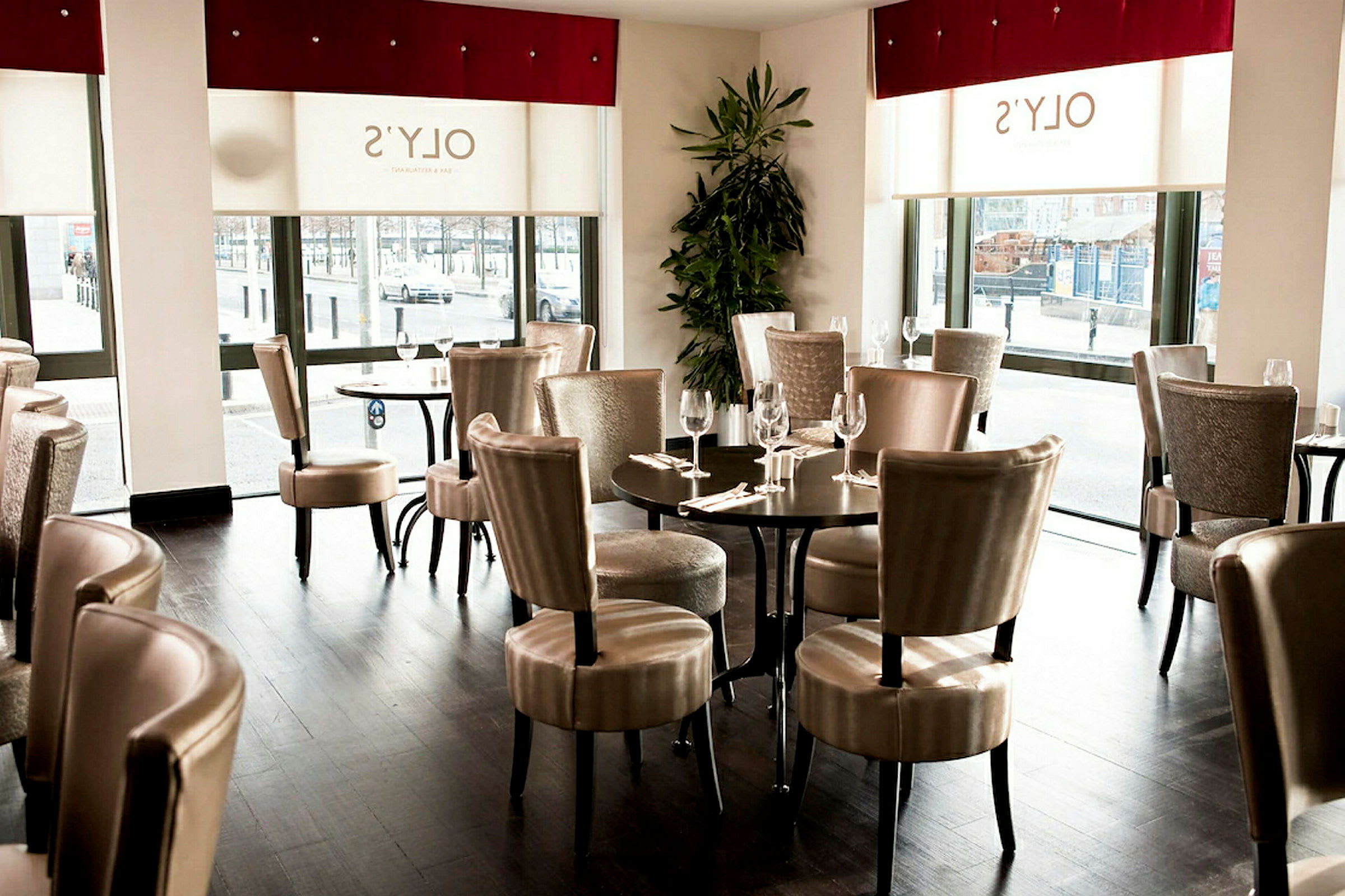 Innendørs i en restaurant med bord og stoler samt store vinduer. (AI-generert tekst)