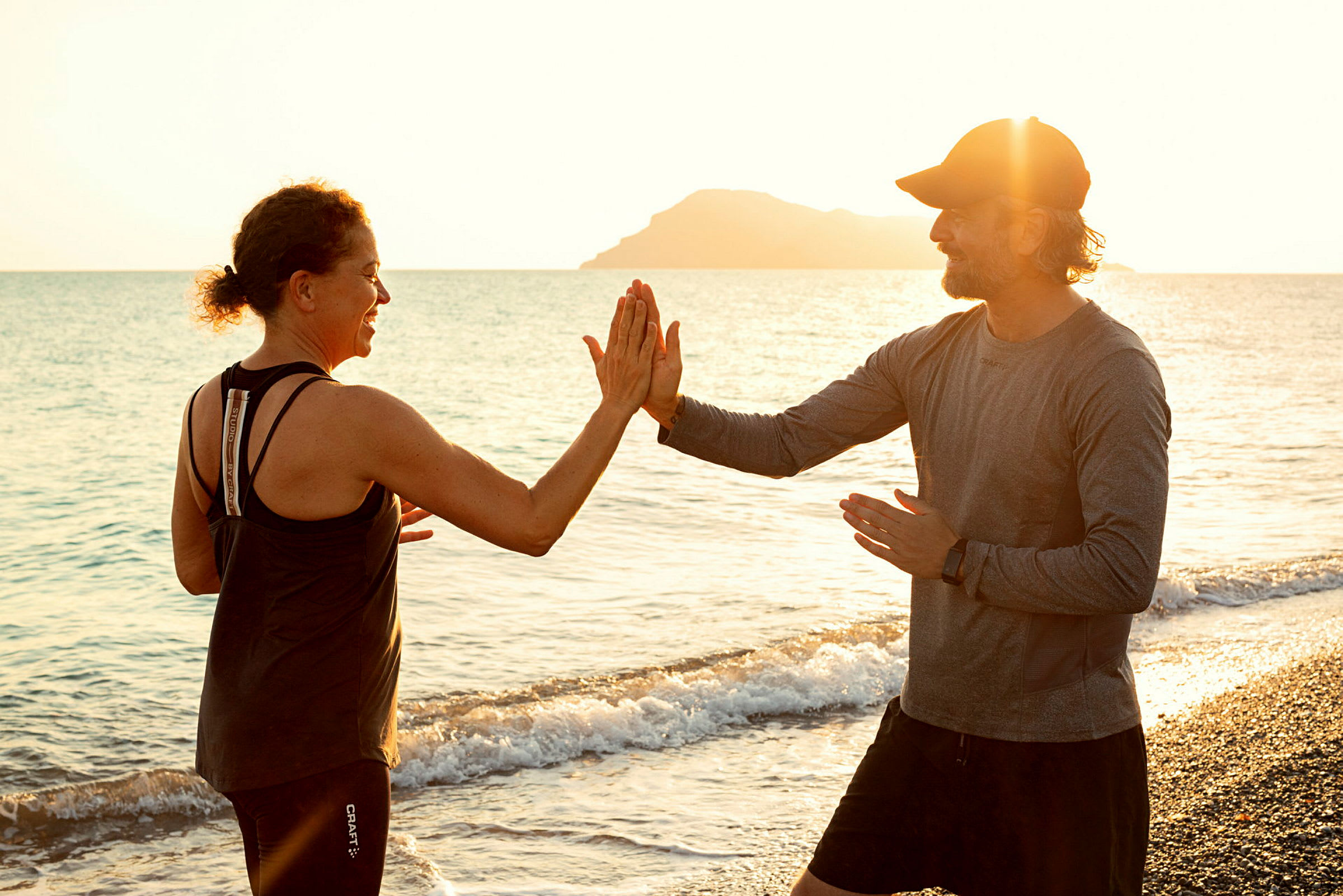 To personer trener ved en strand med solnedgang i bakgrunnen. (AI-generert tekst)