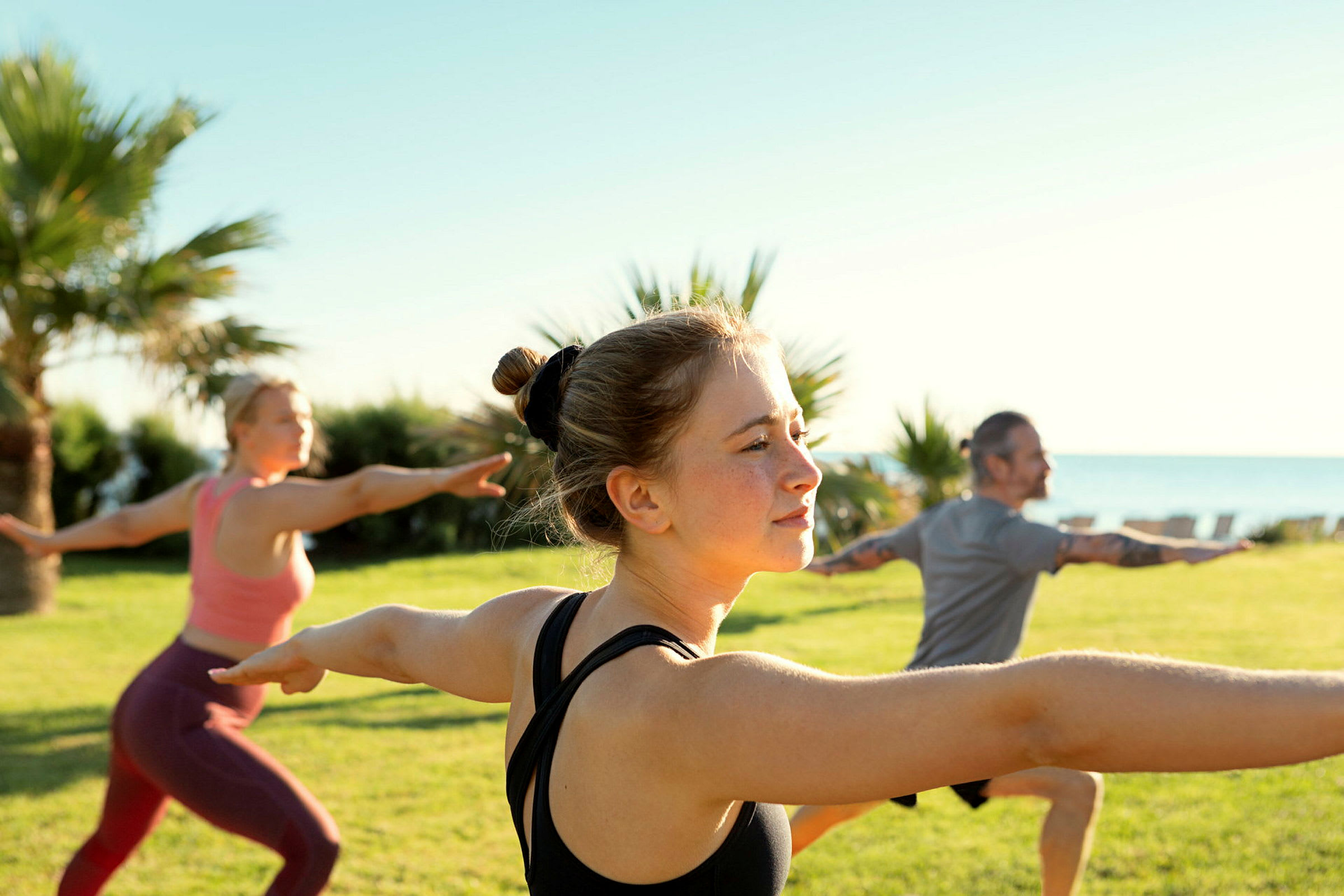 Personer som utfører yoga i en grønn park med havet i bakgrunnen. (AI-generert tekst)