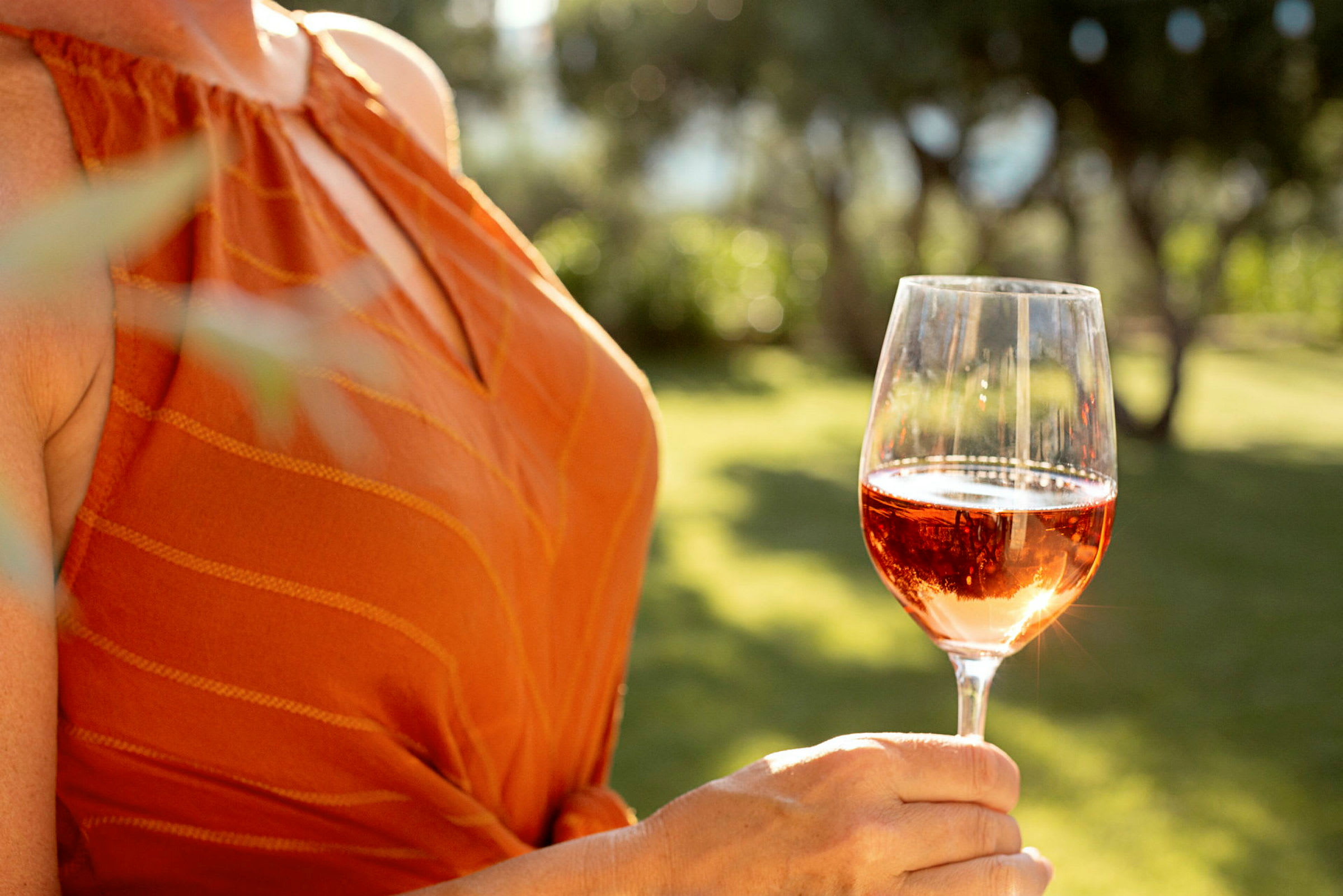En person holder et glass rosévin utendørs. (AI-generert tekst)