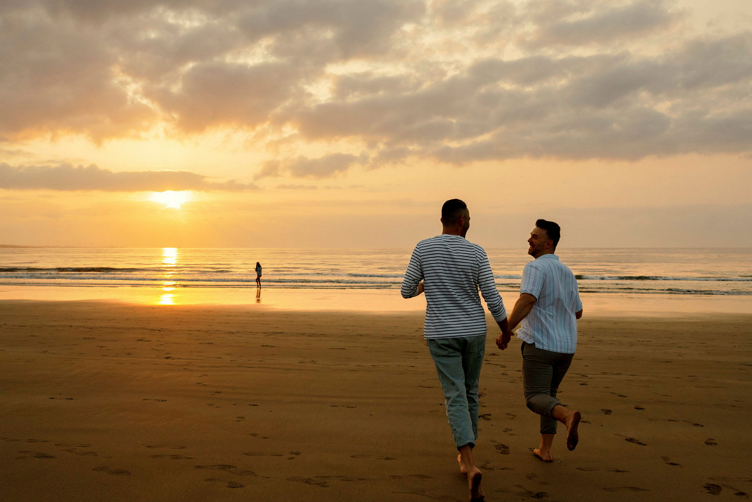 To personer holder hender mens de går på en strand ved solnedgang. (AI-generert tekst)