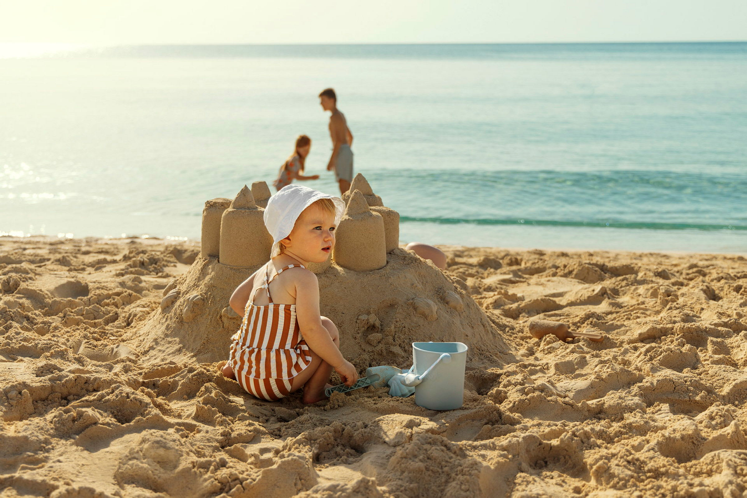 Barn som bygger et sandslott på stranden med en bøtte ved siden av. (AI-generert tekst)