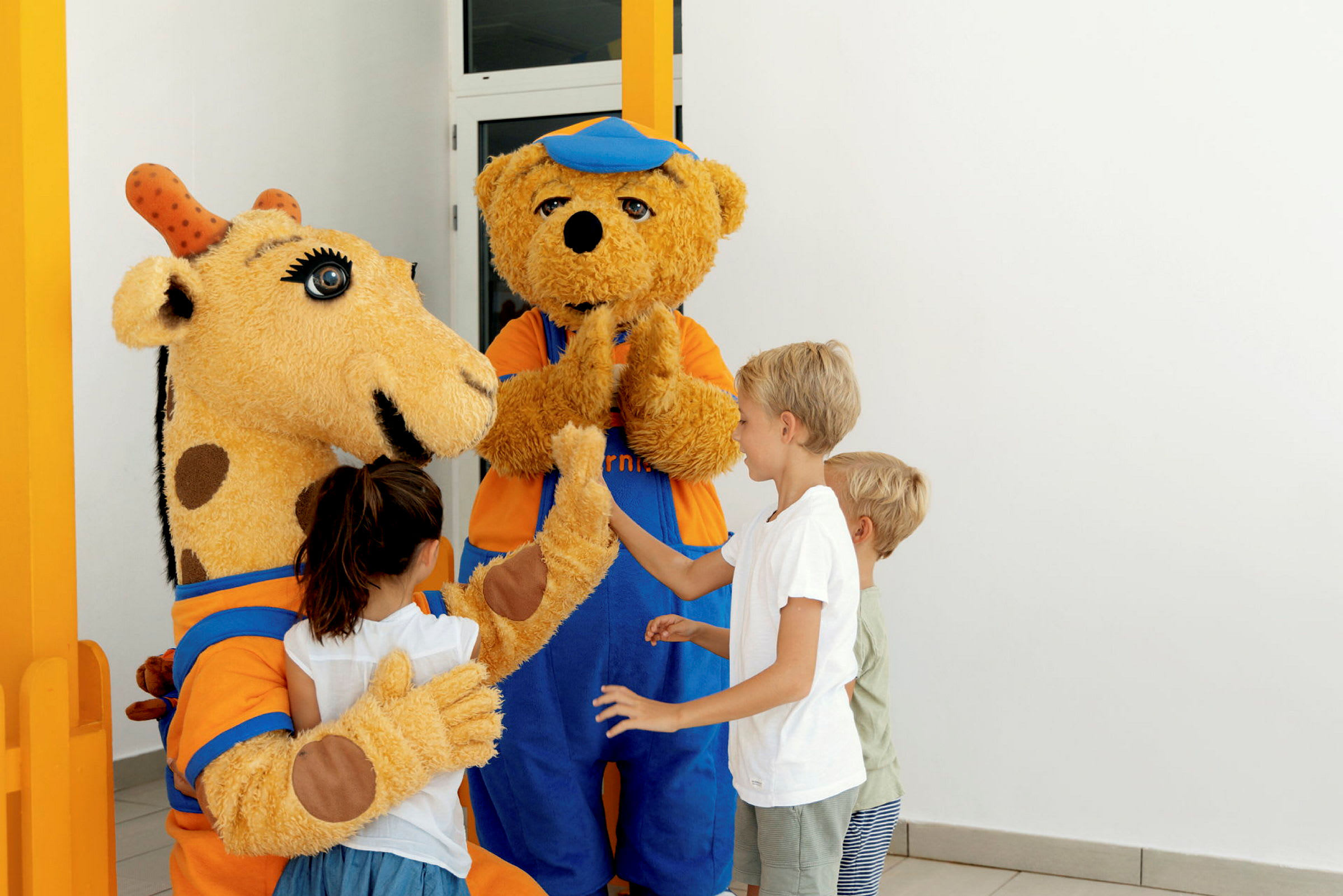 Barn hilser på to figurer i kostyme, en giraff og en bjørn. (AI-generert tekst)